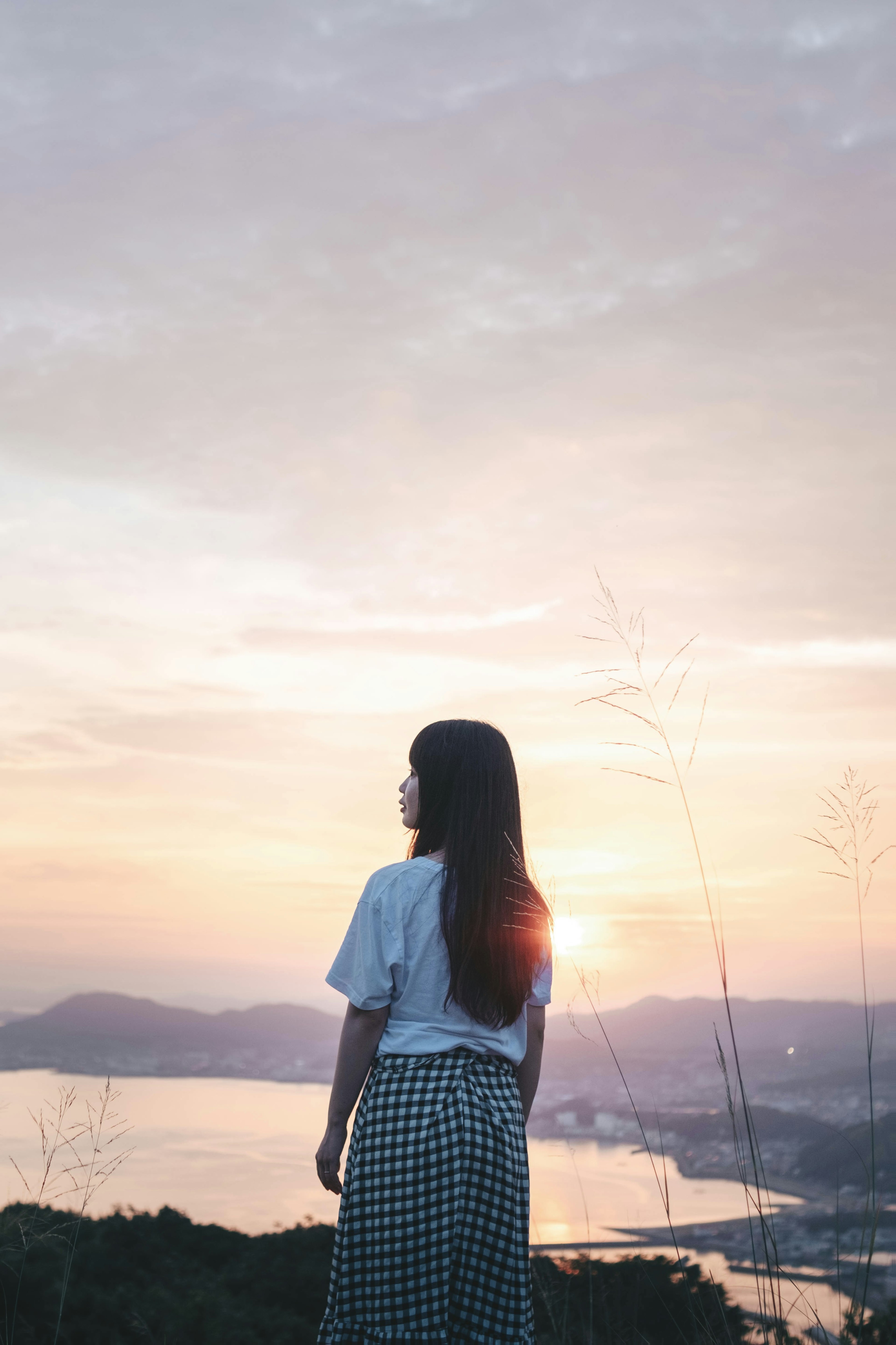 夕日を背にした女性が山の頂上で立っている