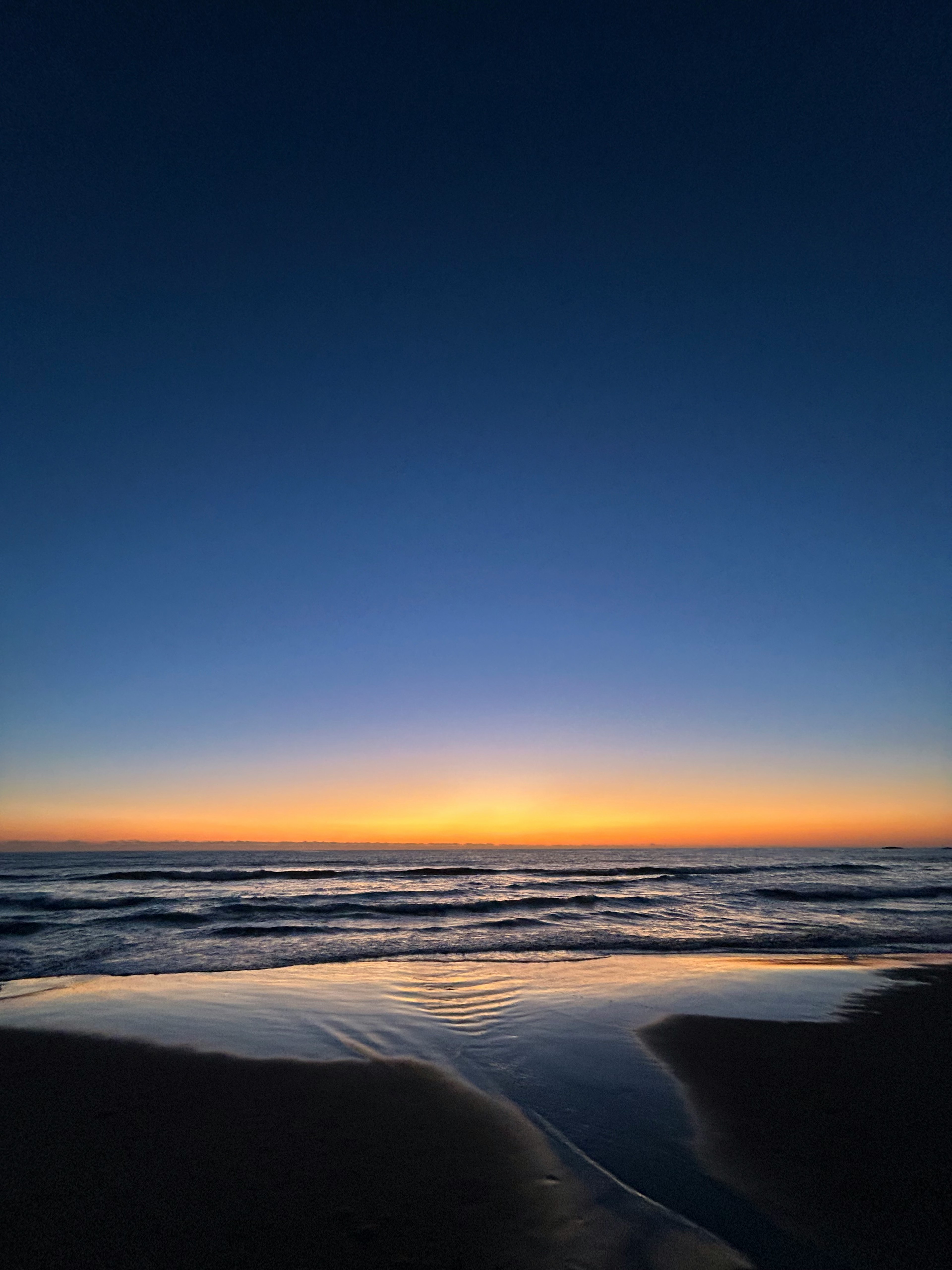 海岸の夕暮れの風景 水面に映るオレンジと青のグラデーション