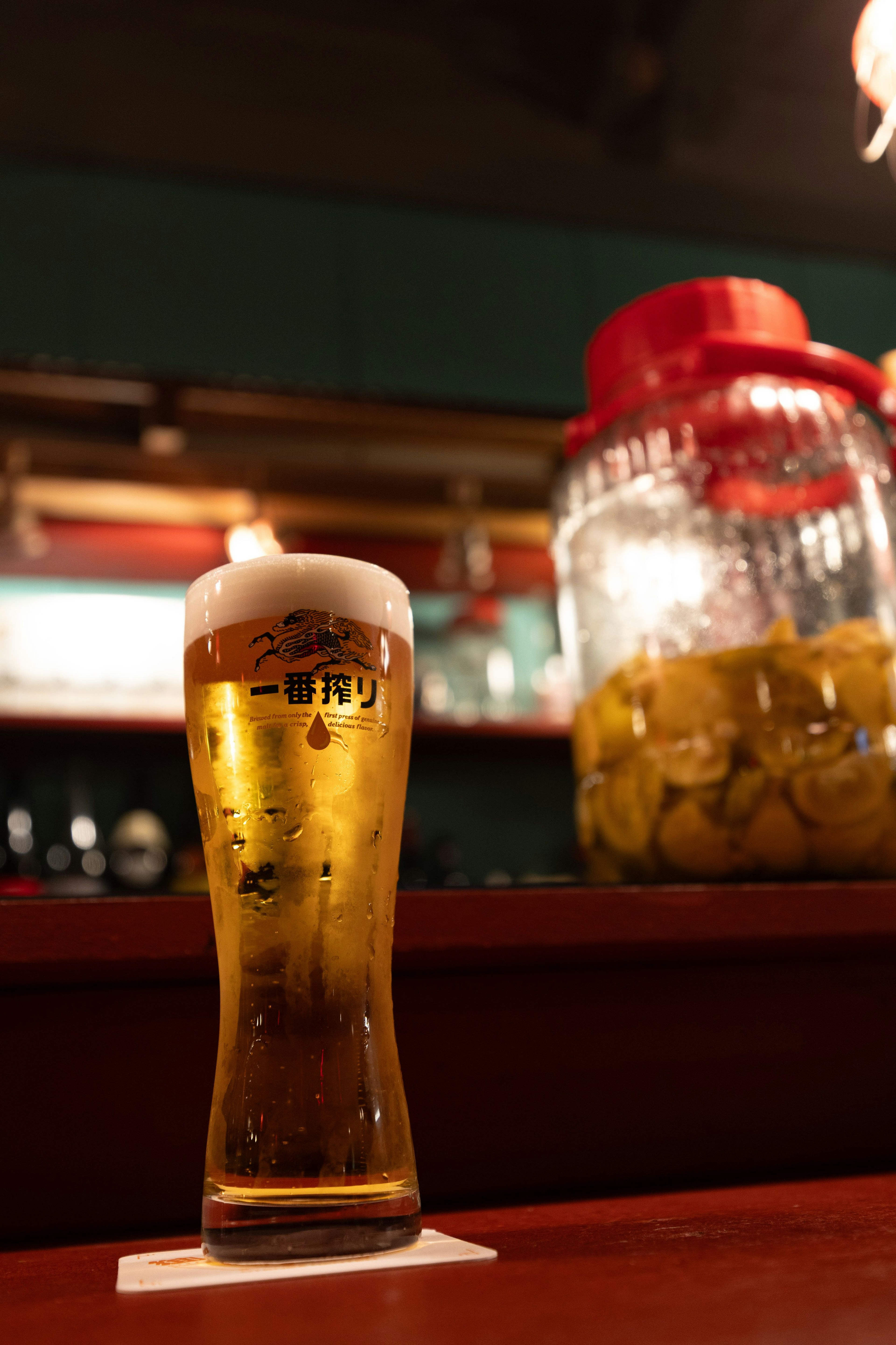 Ein Glas Bier auf einer Bar-Theke mit einem großen Obstglas im Hintergrund