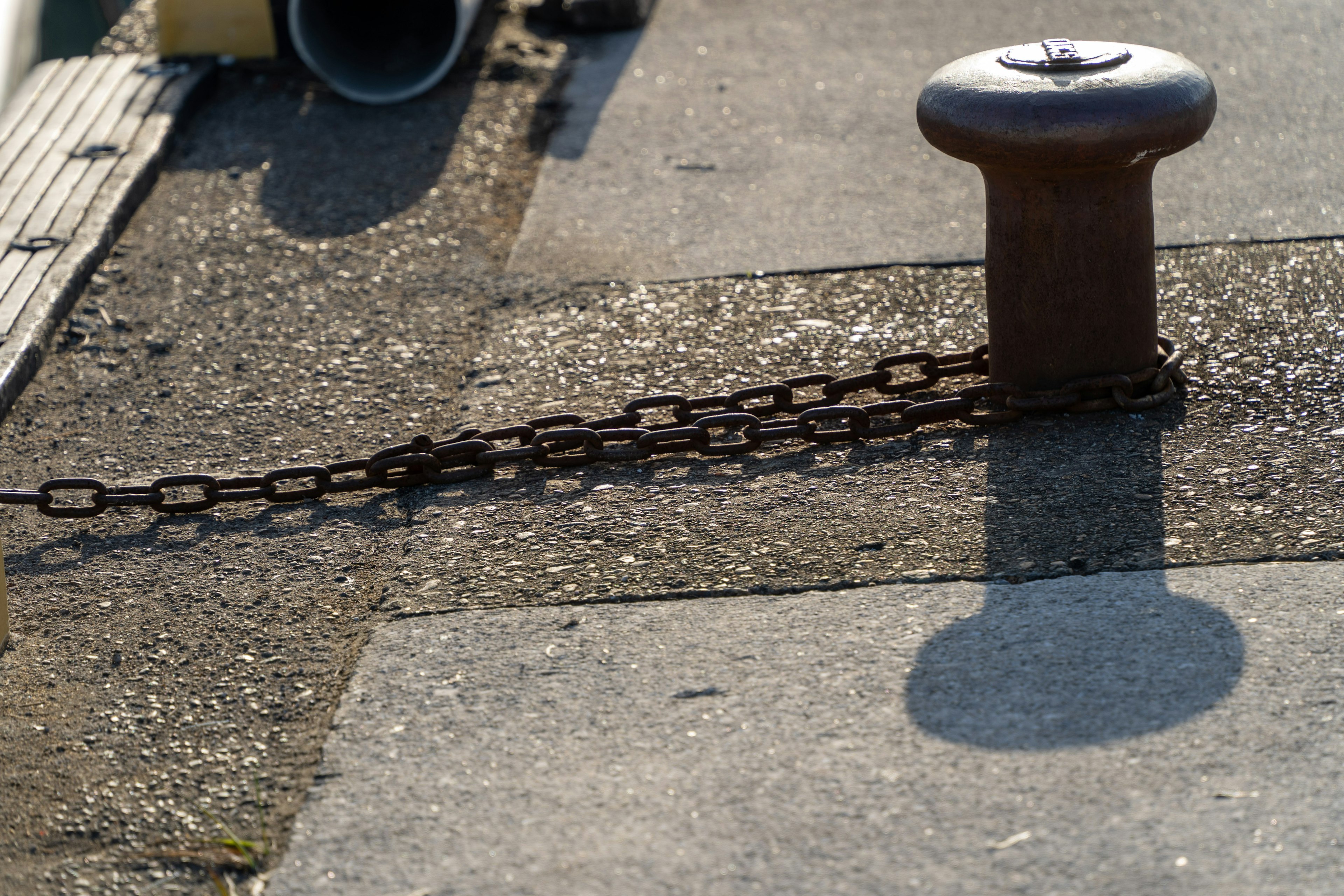 Un bollard en métal avec une chaîne sur une surface en béton au port