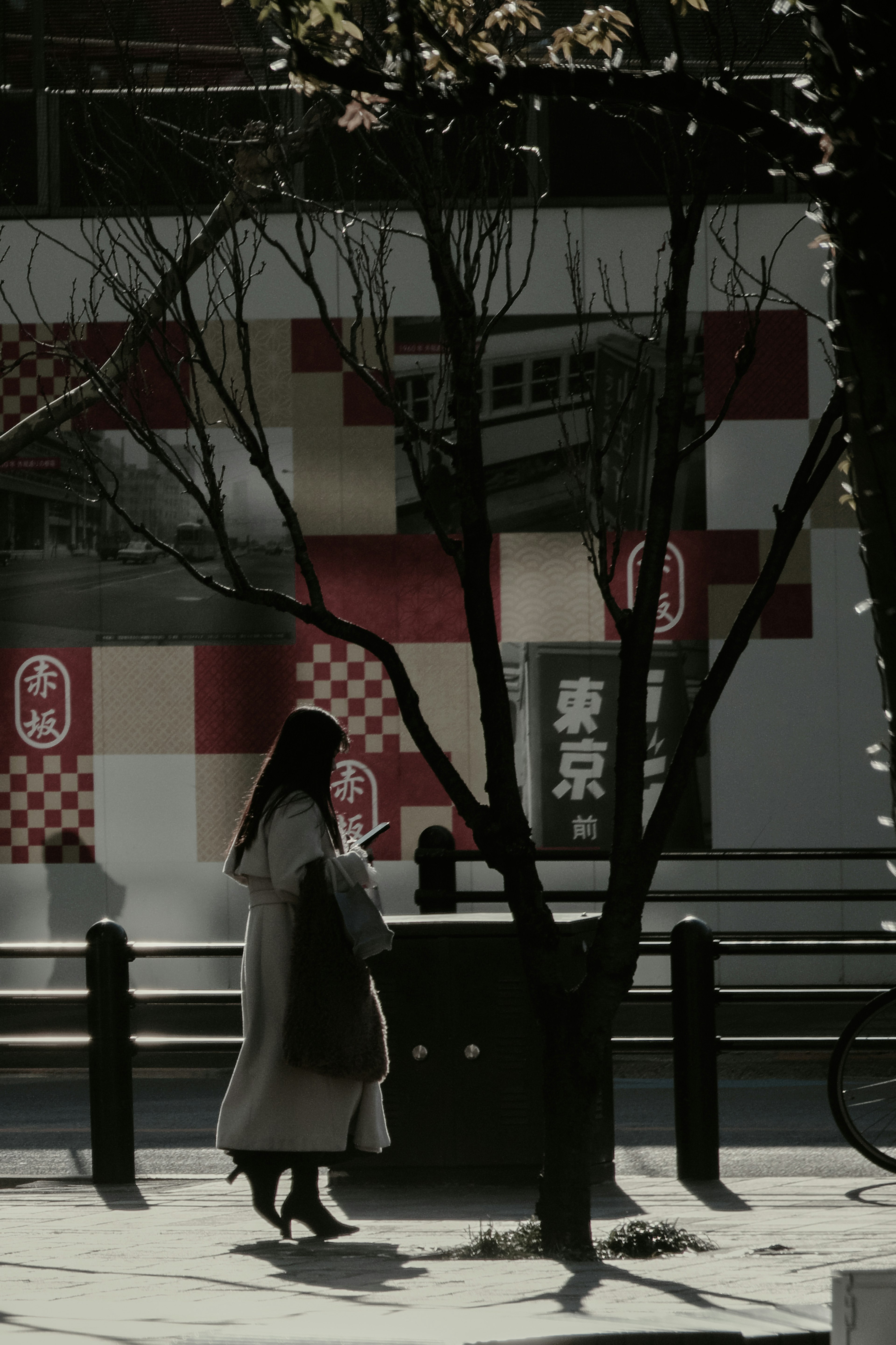 A woman walking between trees in a Tokyo street scene