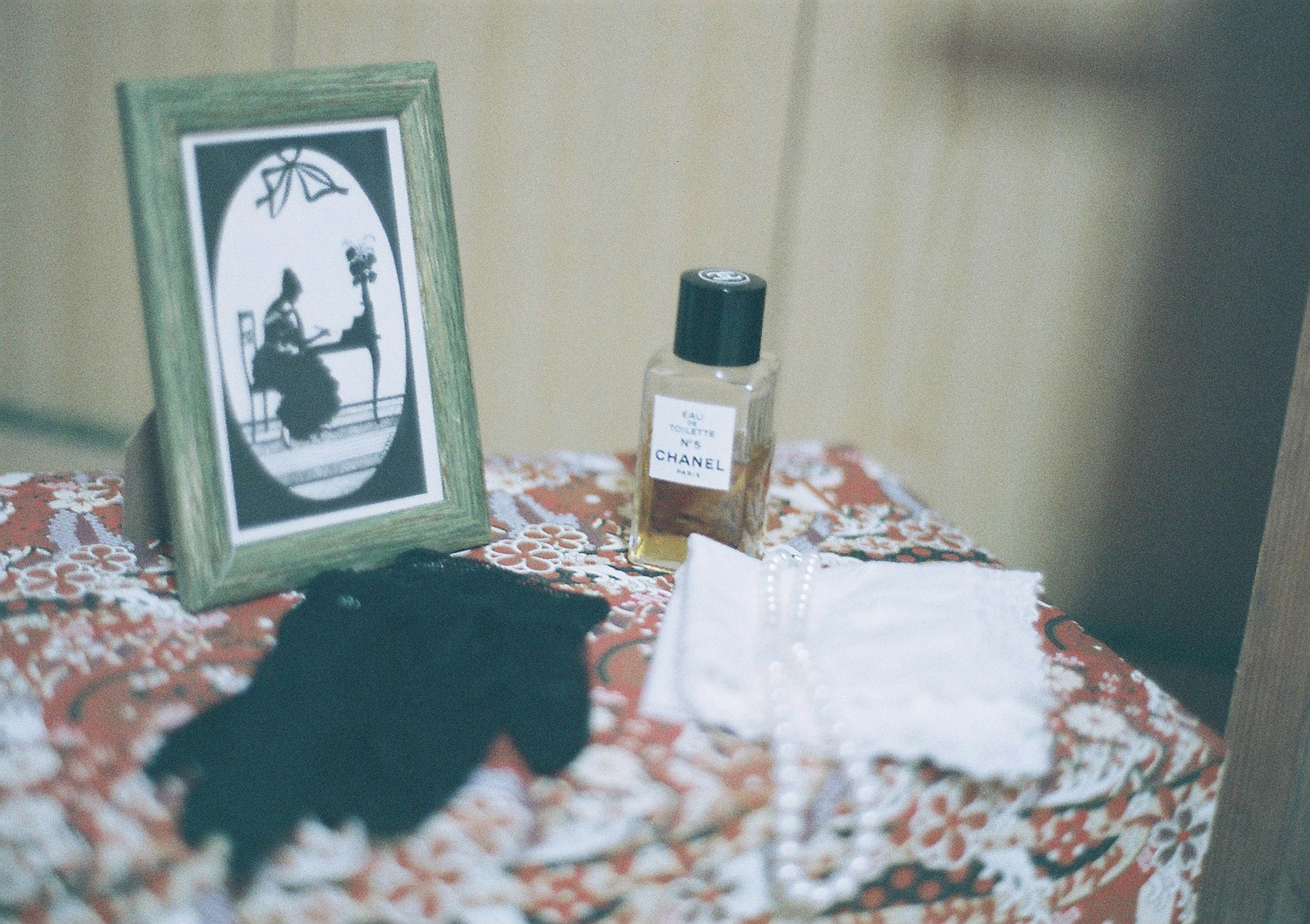 A framed silhouette of a woman on a table with black gloves and a bottle of perfume