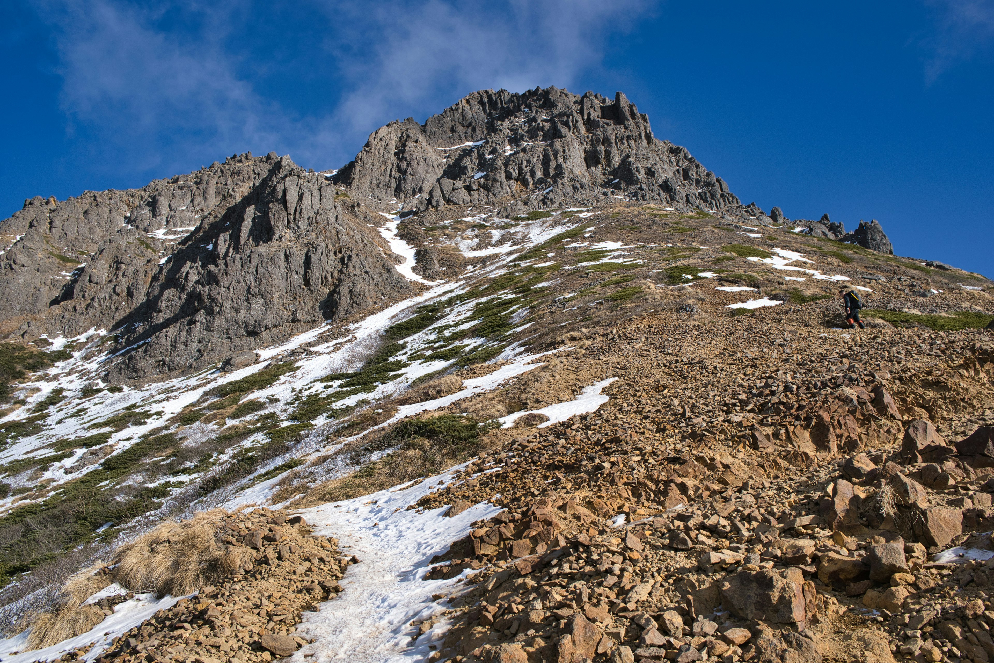 Paesaggio montano roccioso con macchie di neve e cielo blu