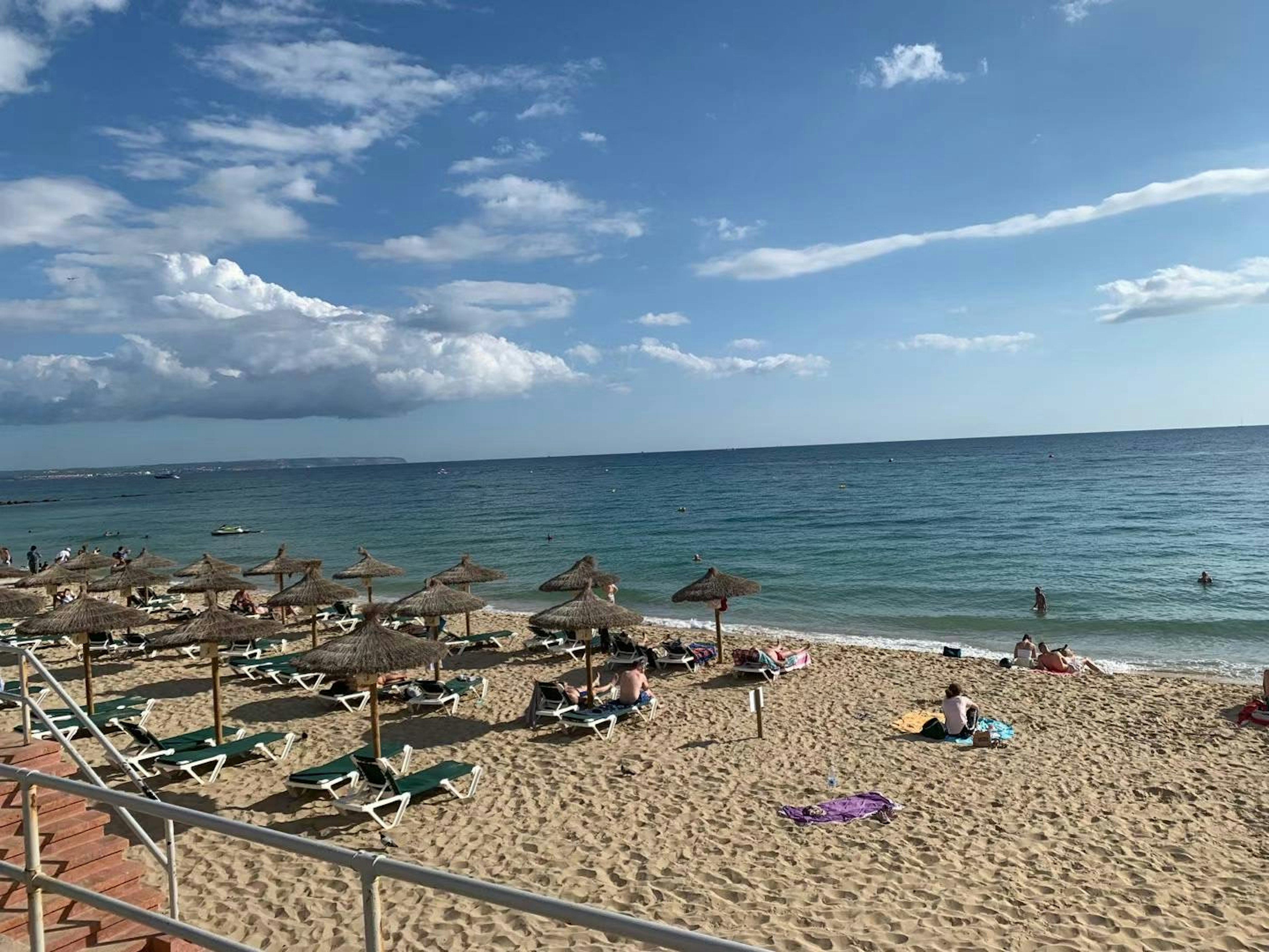 Scena di spiaggia con ombrelloni e lettini sulla sabbia sotto un cielo blu