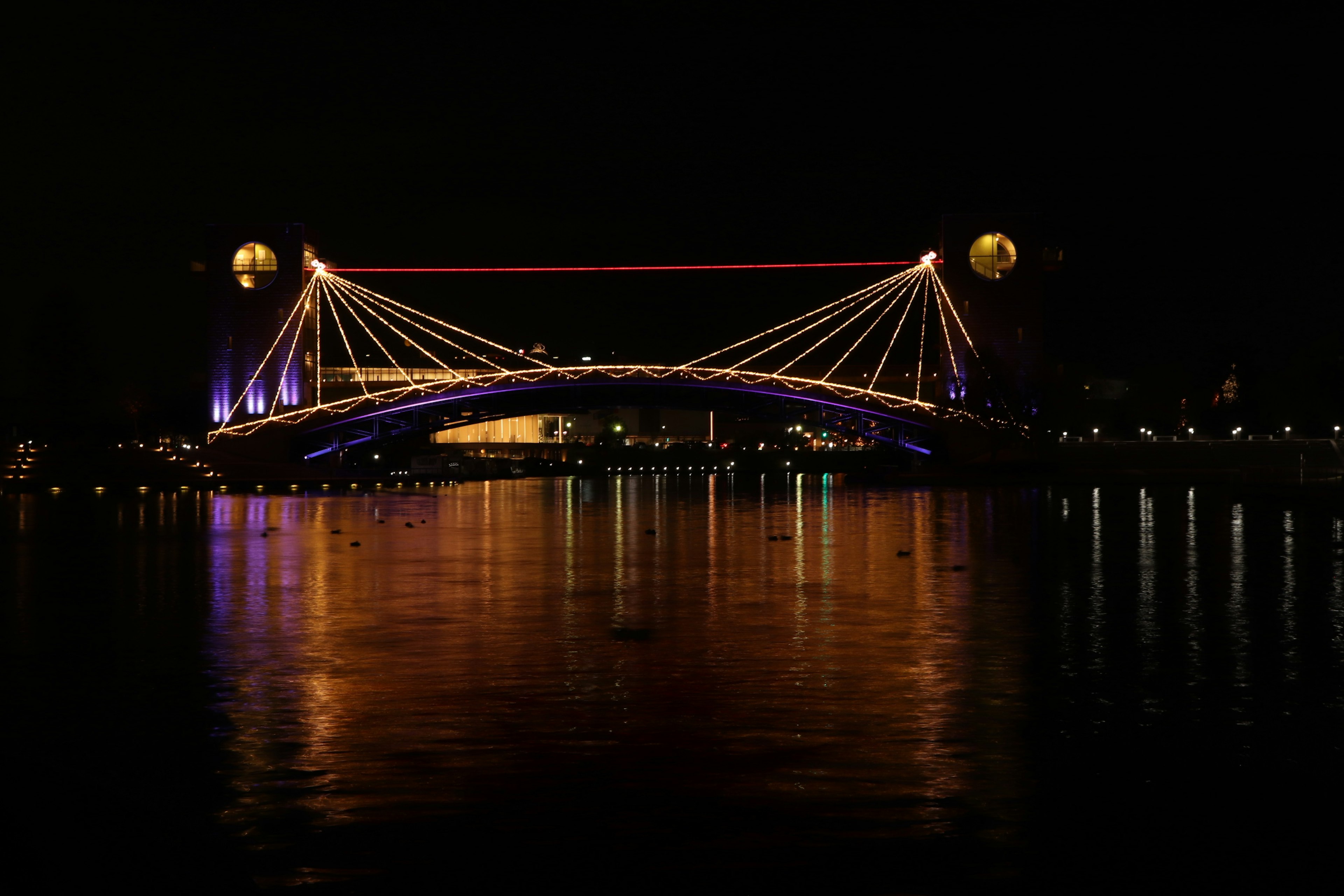 สะพานที่สวยงามส่องสว่างในตอนกลางคืนพร้อมการสะท้อนบนผิวน้ำ