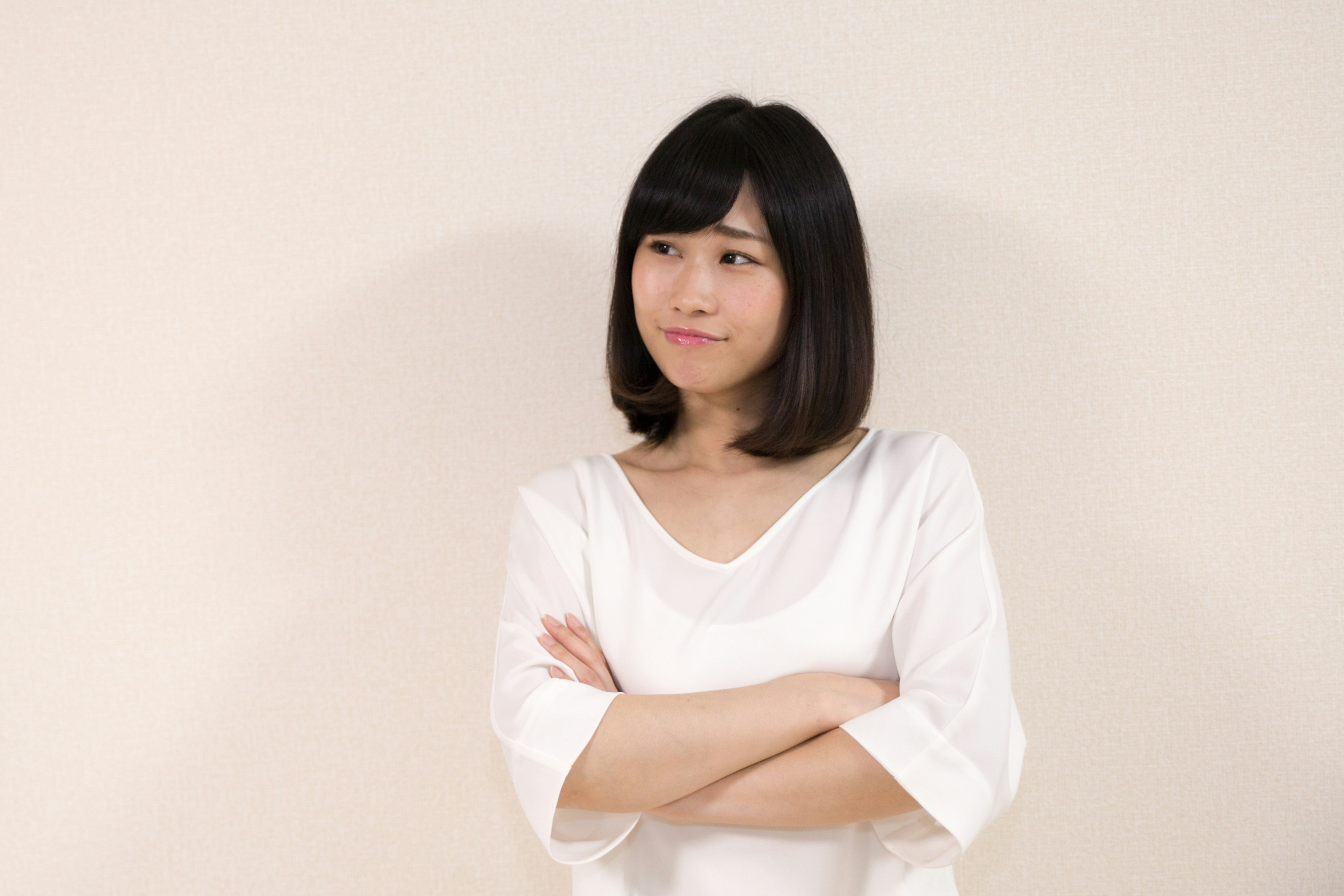 A woman in a white shirt stands with arms crossed