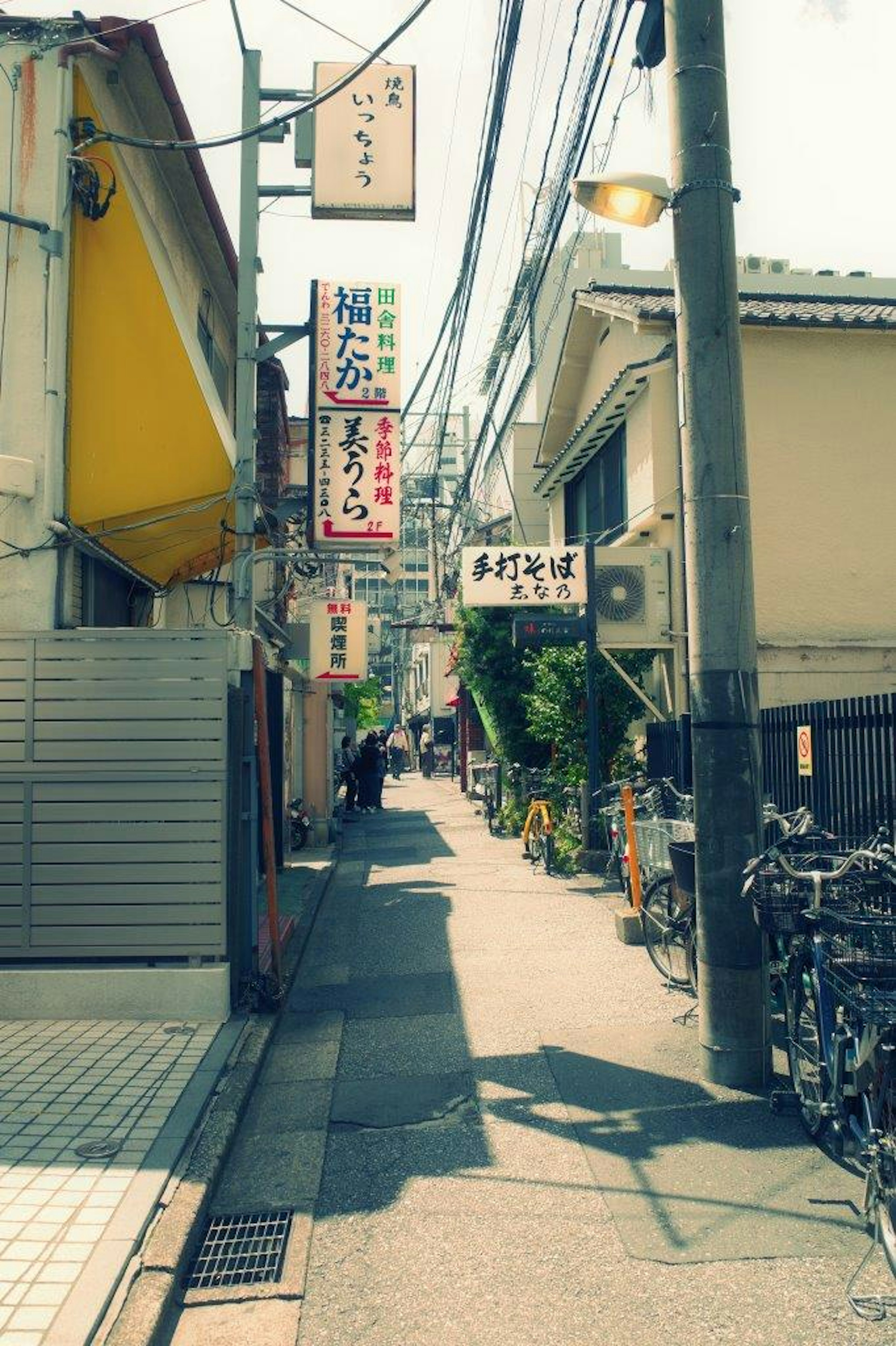 狭い路地に並ぶ飲食店や自転車が見える風景