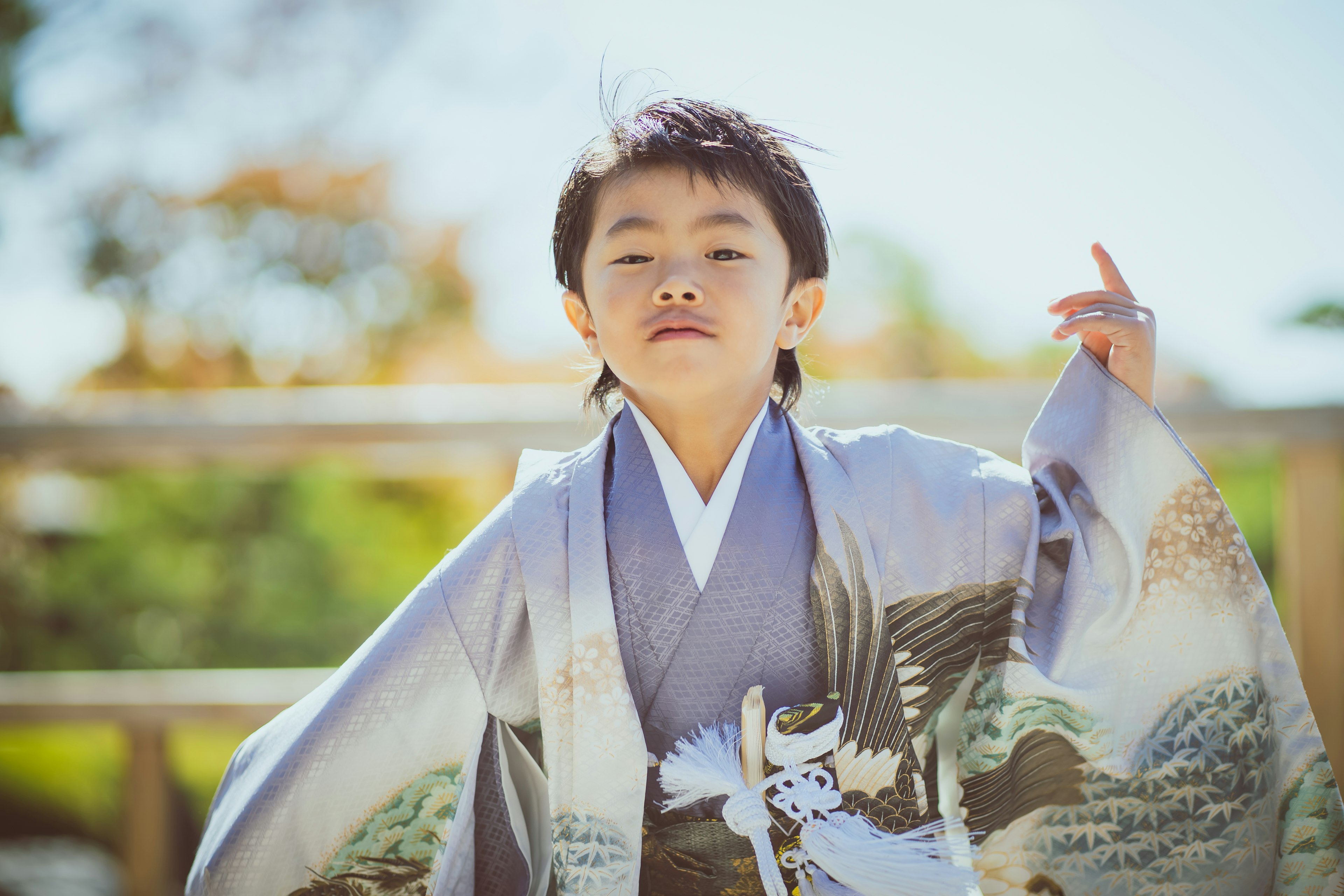 Ein Kind in einem blauen Kimono, das selbstbewusst posiert vor einer natürlichen Landschaft