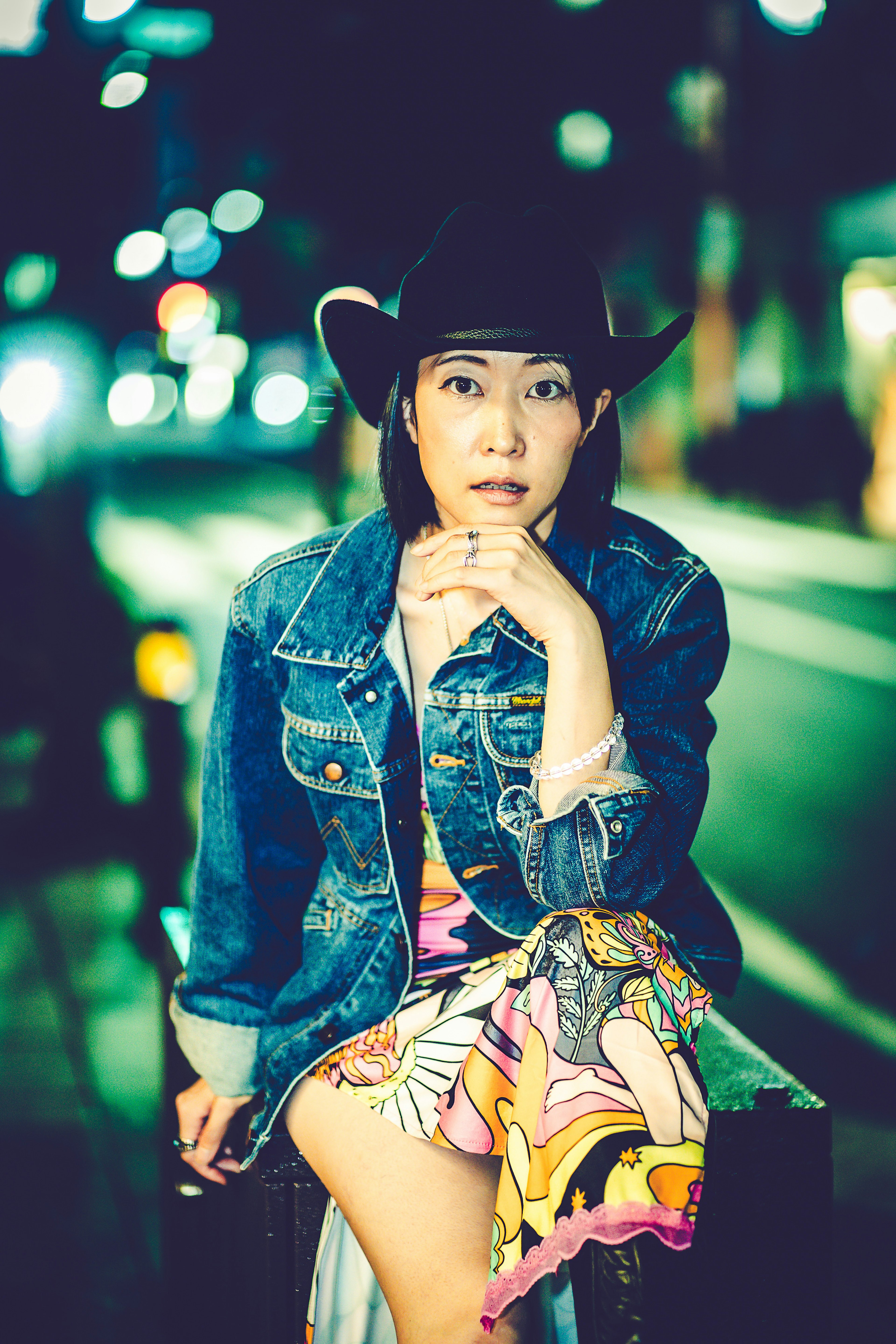 A woman wearing a denim jacket and cowboy hat sitting on a street at night