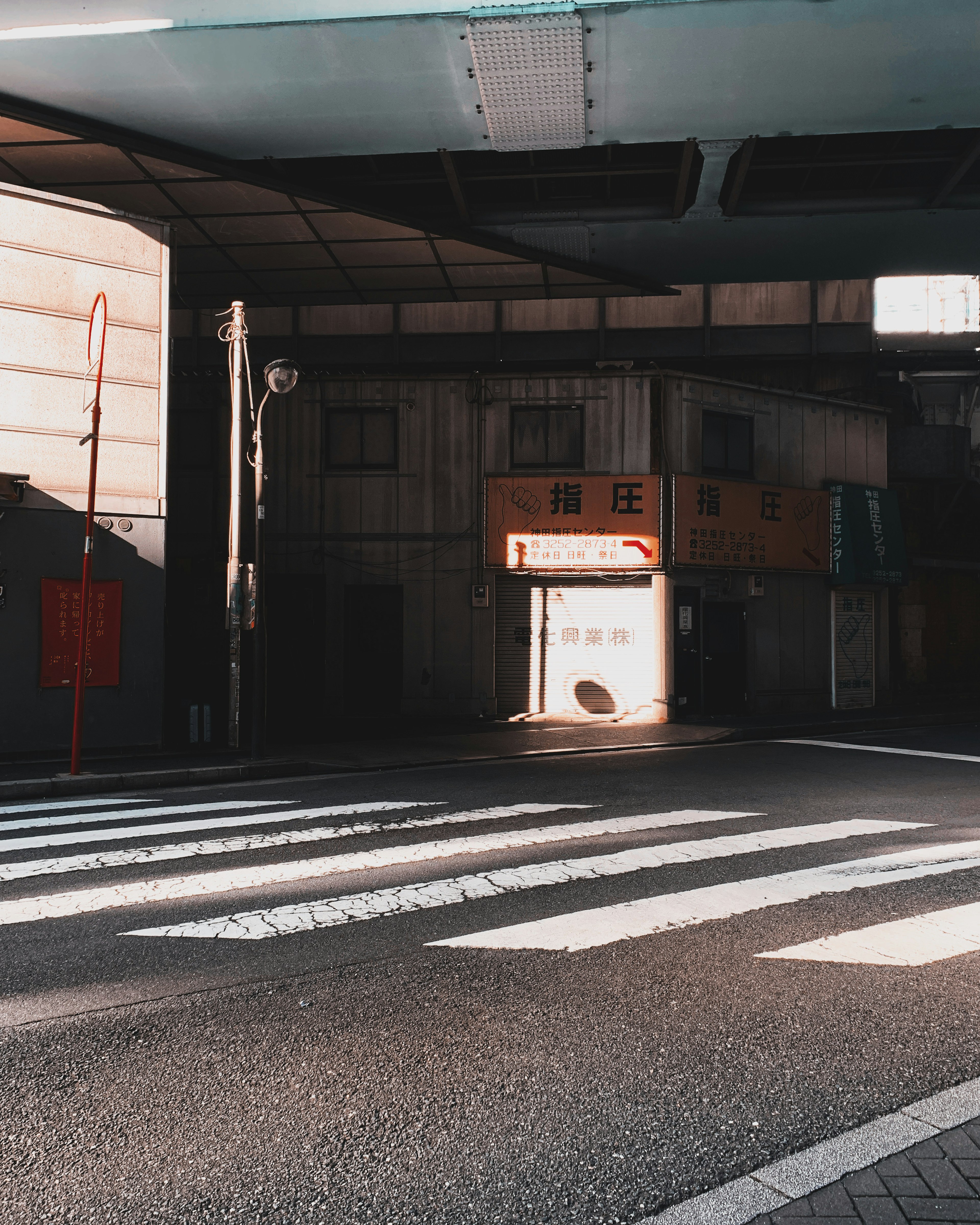 View of a storefront at a crosswalk with shadows and urban architecture