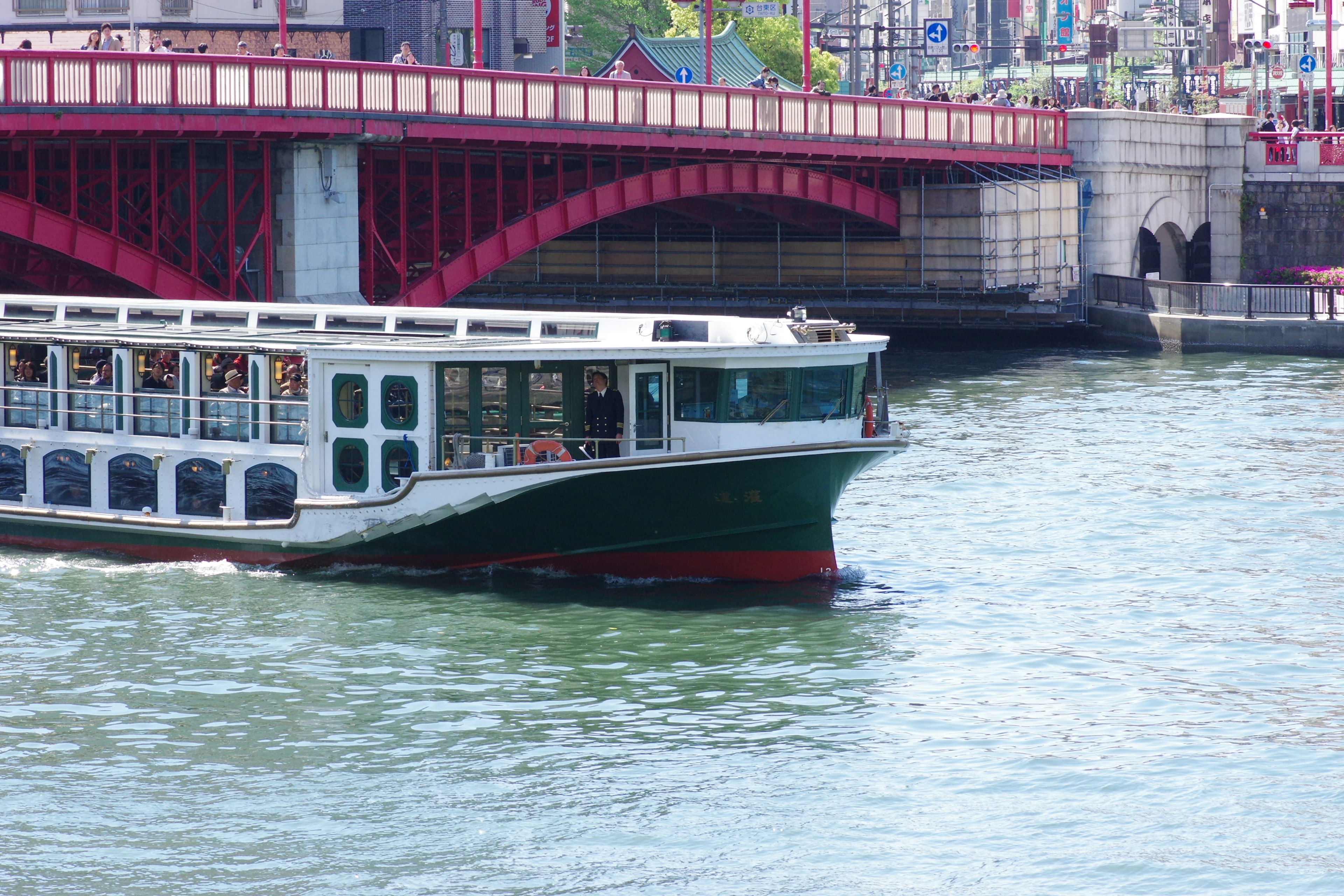 Green boat navigating on the river with a red bridge in the background