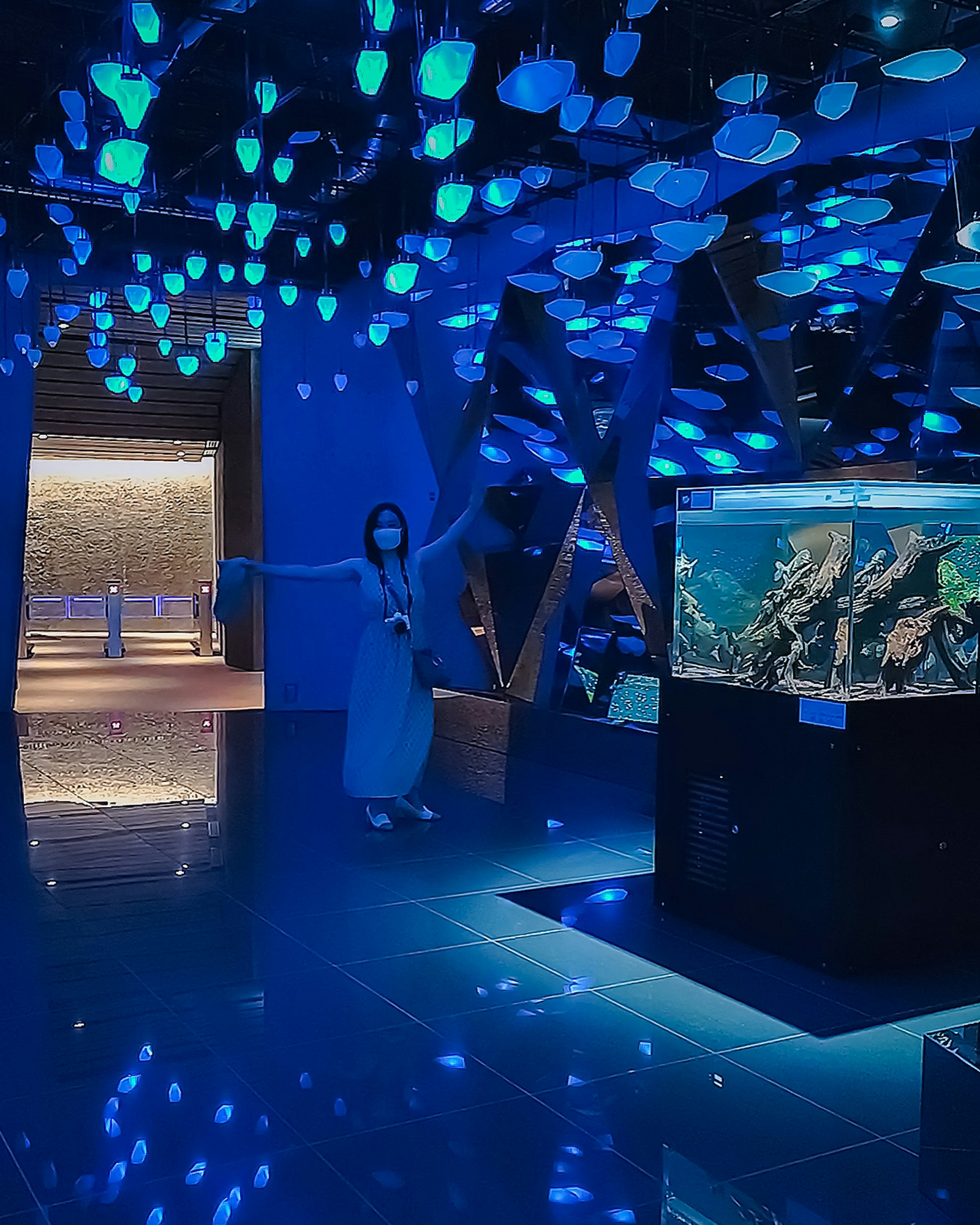 Una mujer disfrutando del interior iluminado del acuario con luces azules y elementos decorativos