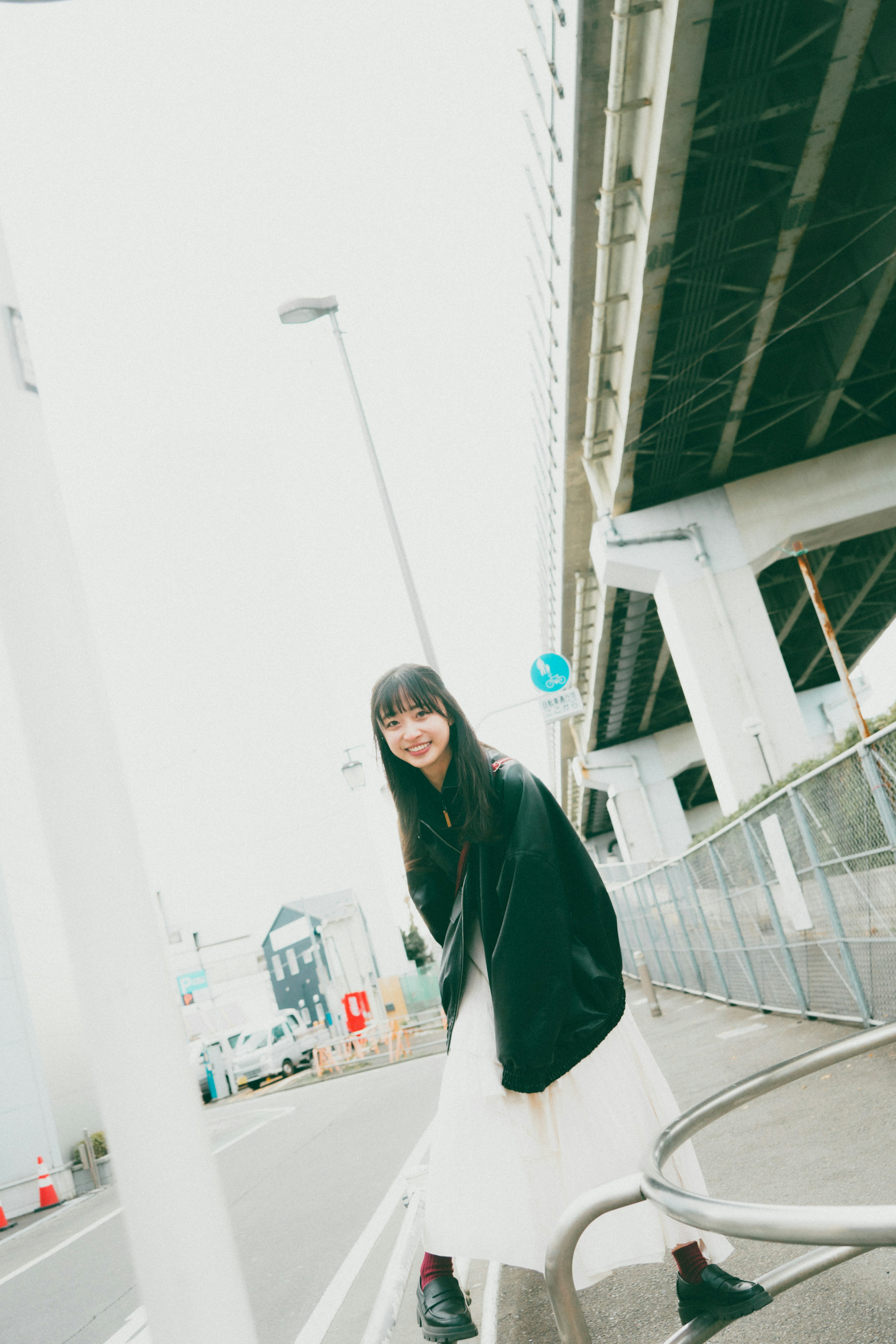 Une femme portant une robe blanche et une veste noire souriant dans un cadre urbain