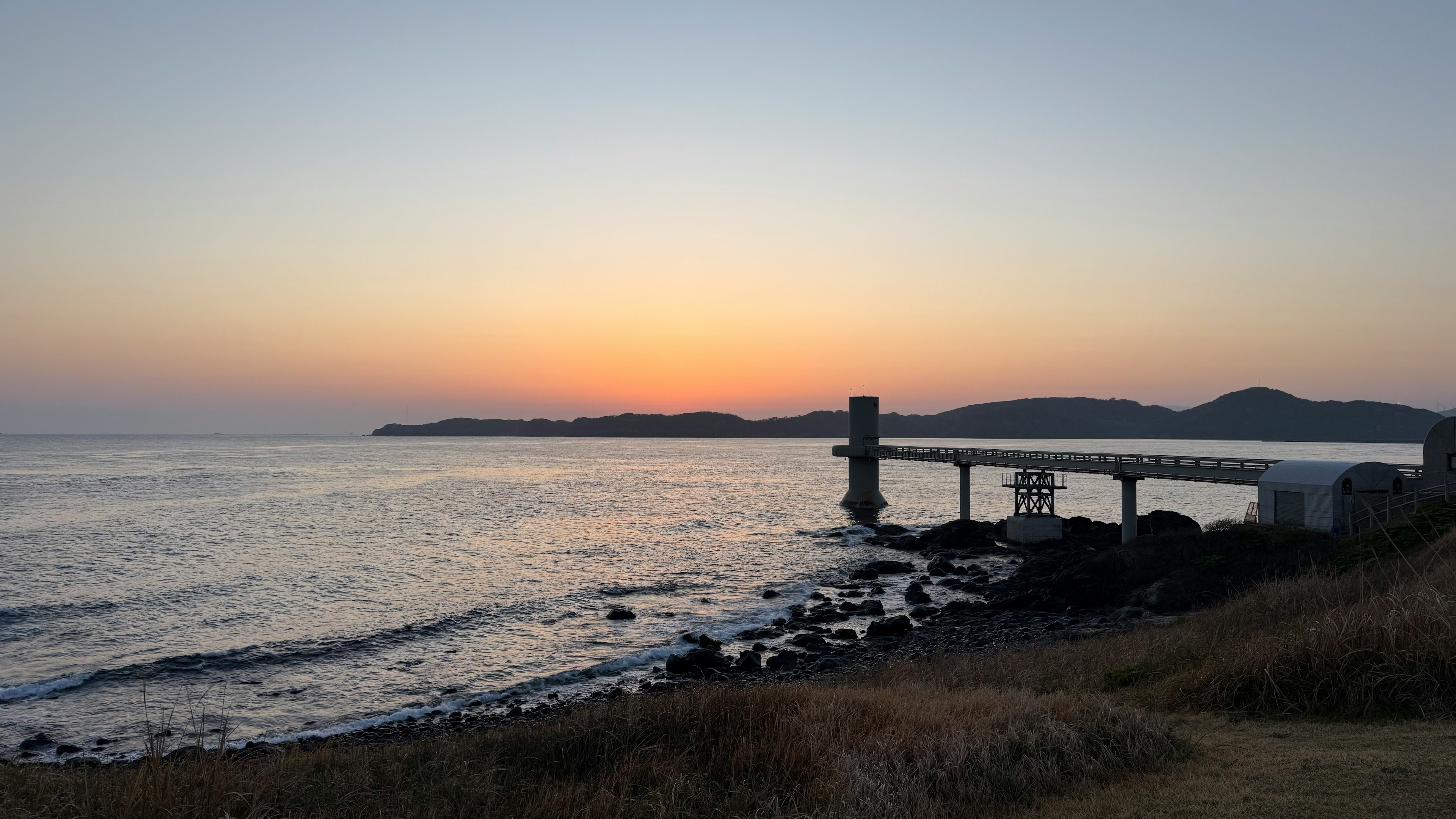 Paisaje costero al atardecer con un puente y olas