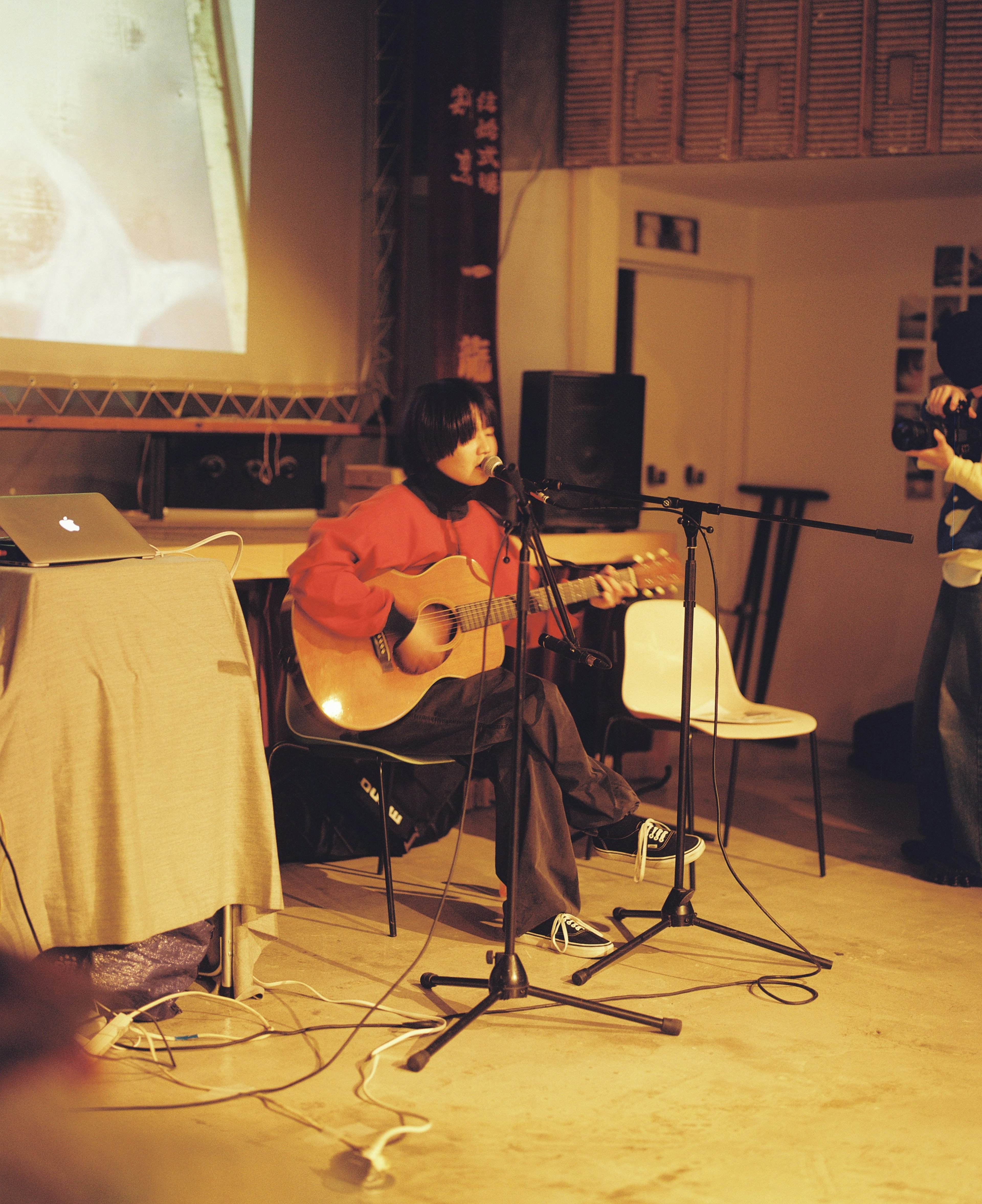 Artist performing with a guitar wearing a red sweater