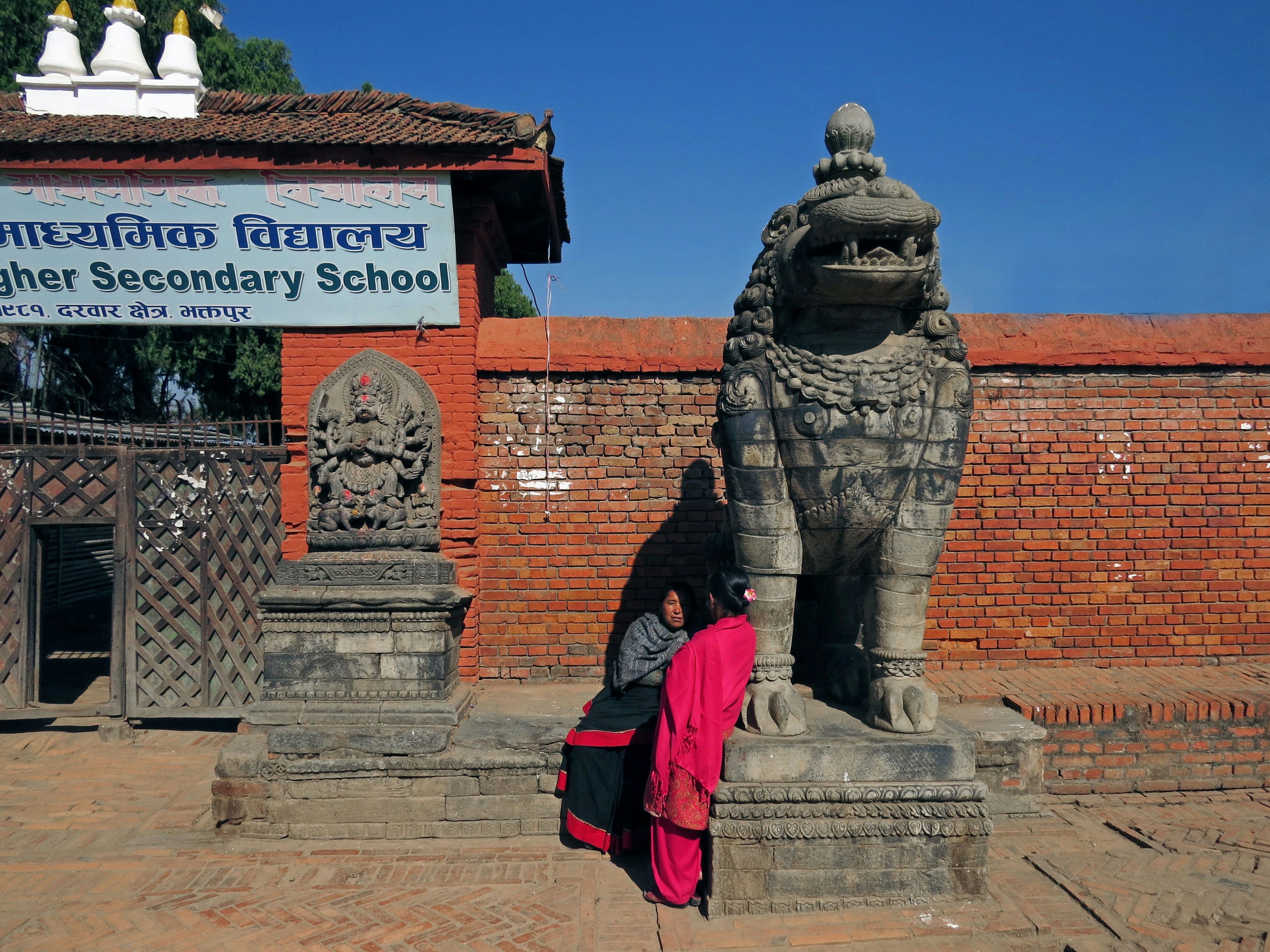 Estatua de león de piedra frente a una escuela con una mujer vestida de rojo