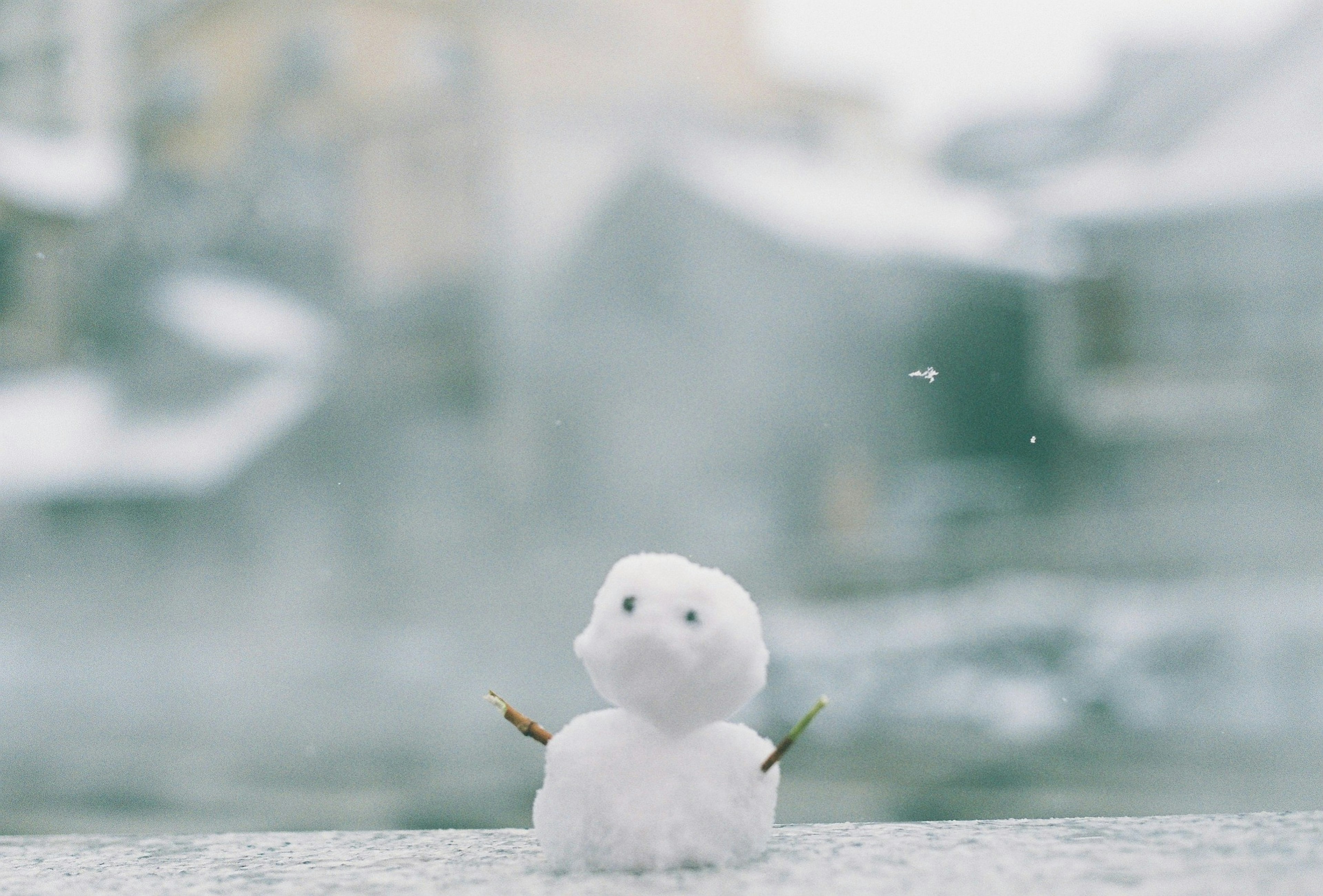 Small snowman standing in snow with blurred winter scenery in background