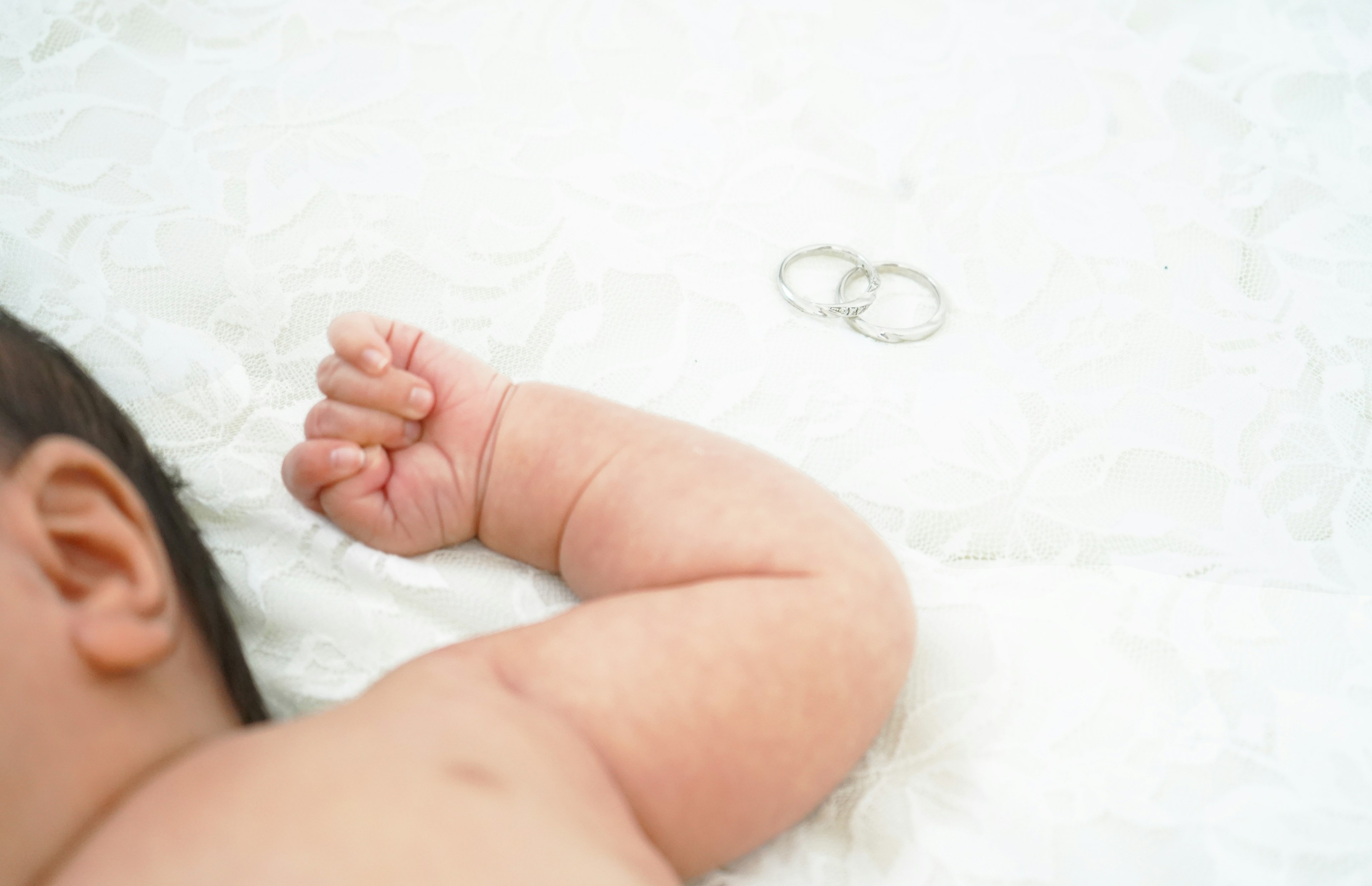 Close-up of a baby's arm with wedding rings nearby