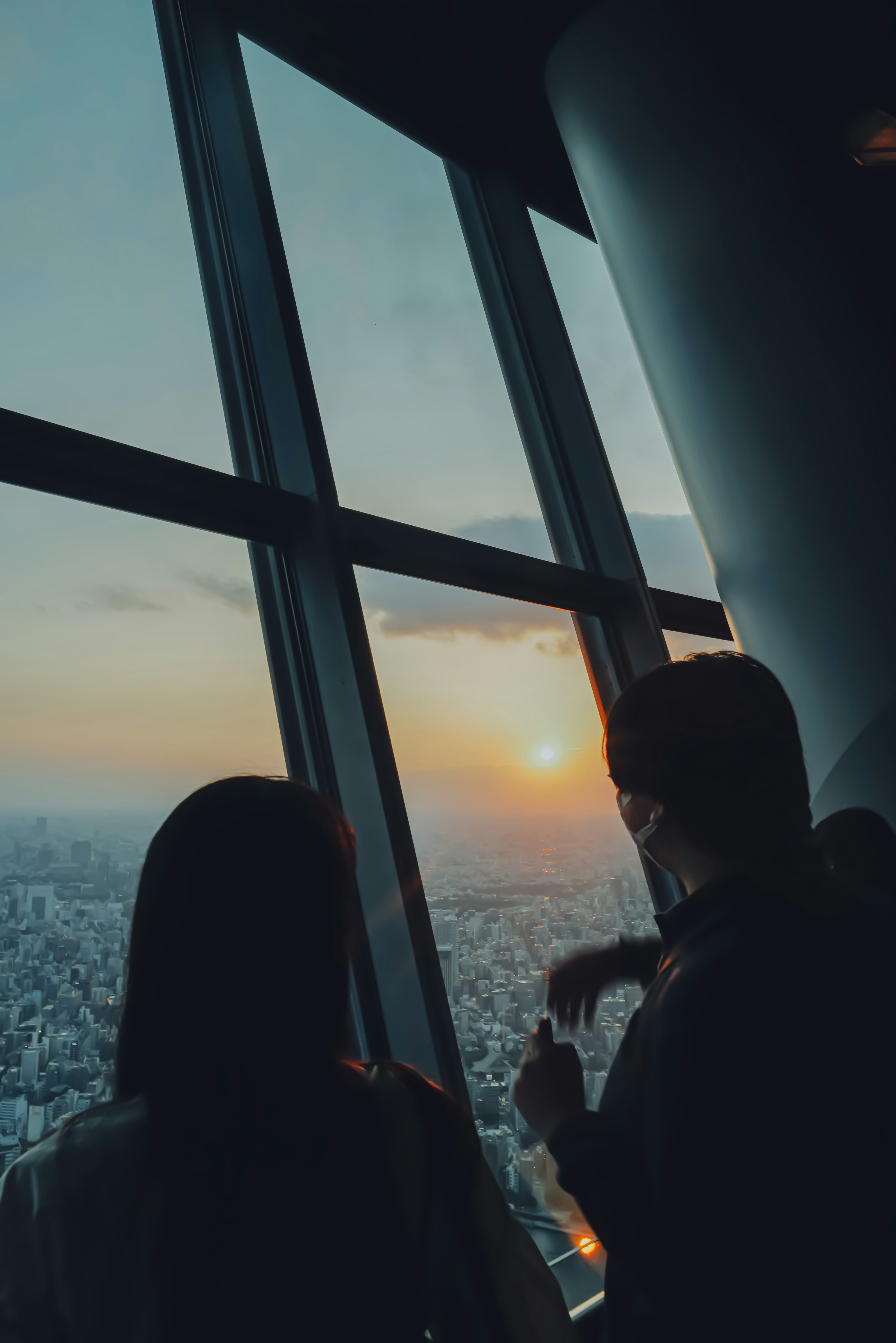 Silueta de dos personas mirando la puesta de sol a través de una ventana de rascacielos