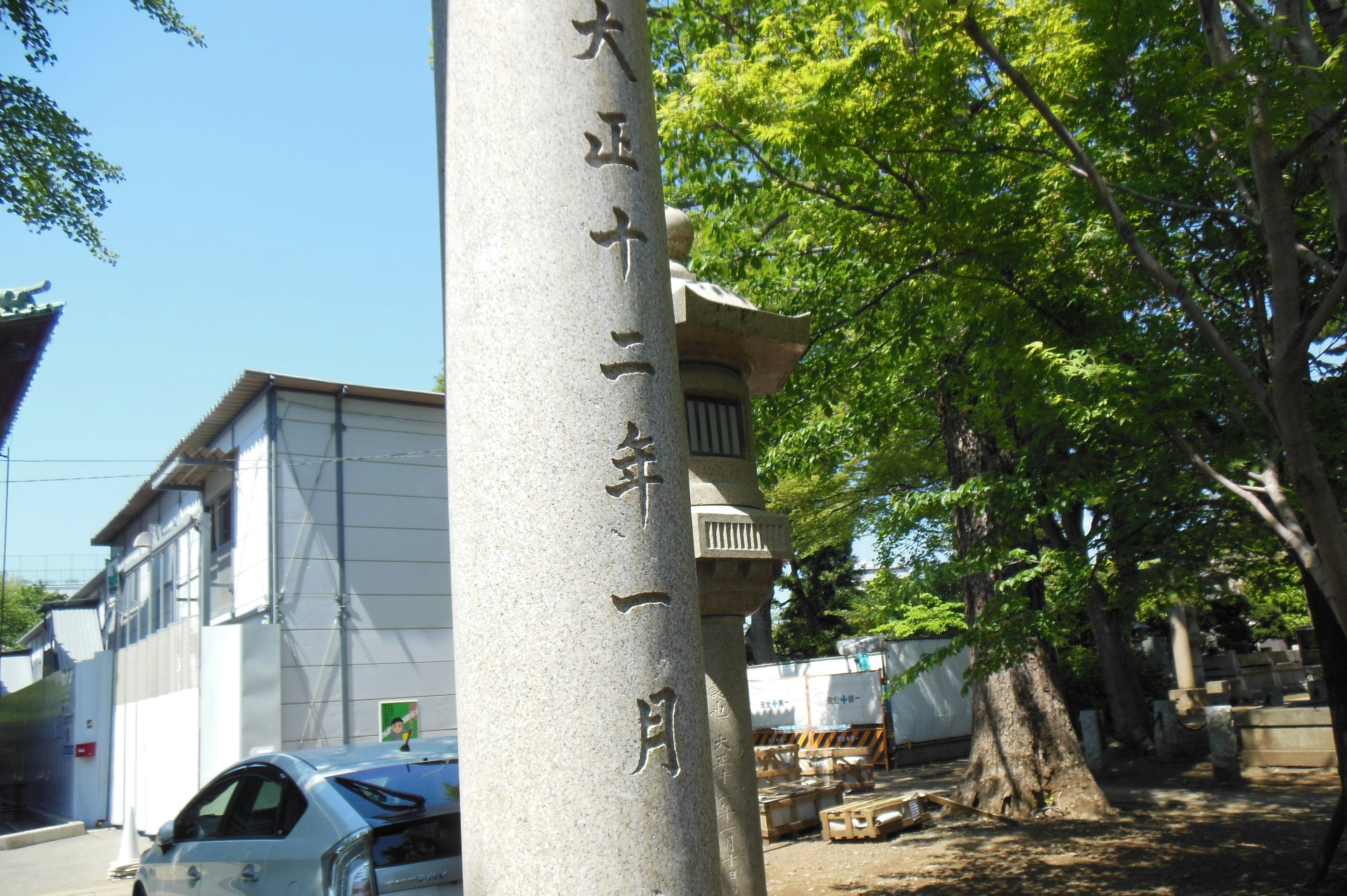 Steinmonument mit japanischen Inschriften umgeben von Bäumen und Gebäuden