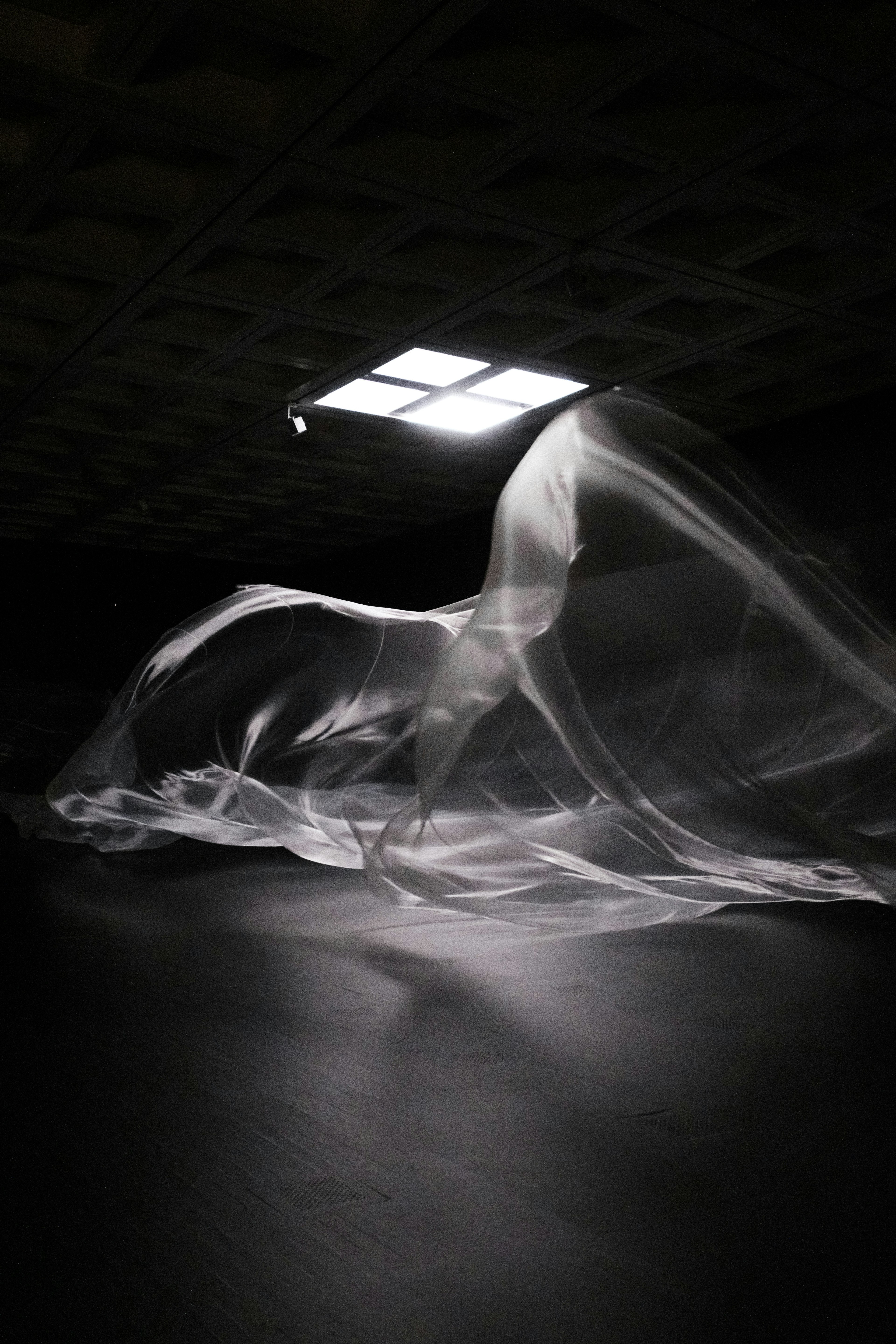 A sheer fabric flowing in a dimly lit space with a bright light source above