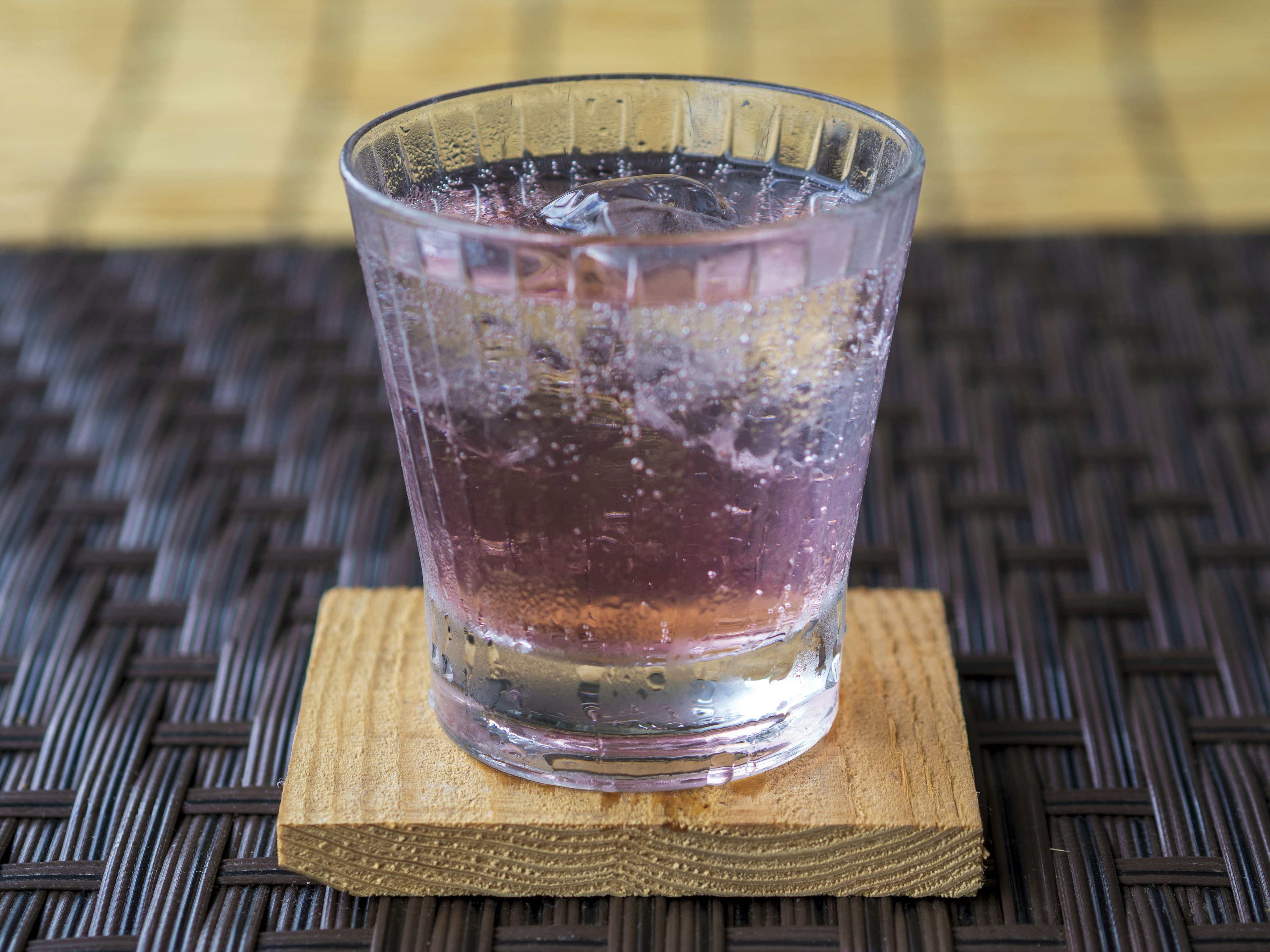 A transparent glass with a purple drink on a wooden coaster placed on a table