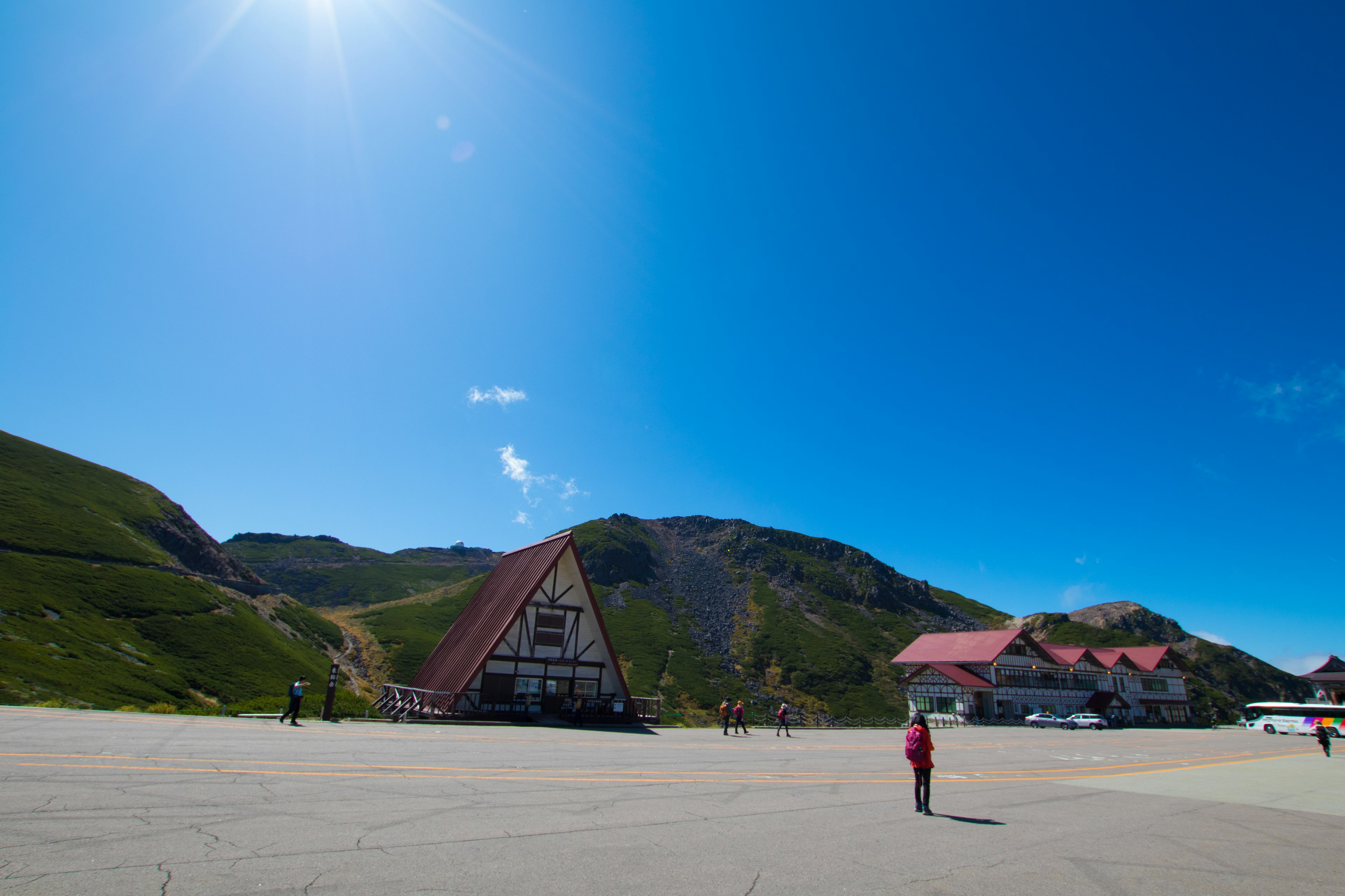 A person standing in a wide open area surrounded by green hills under a clear blue sky