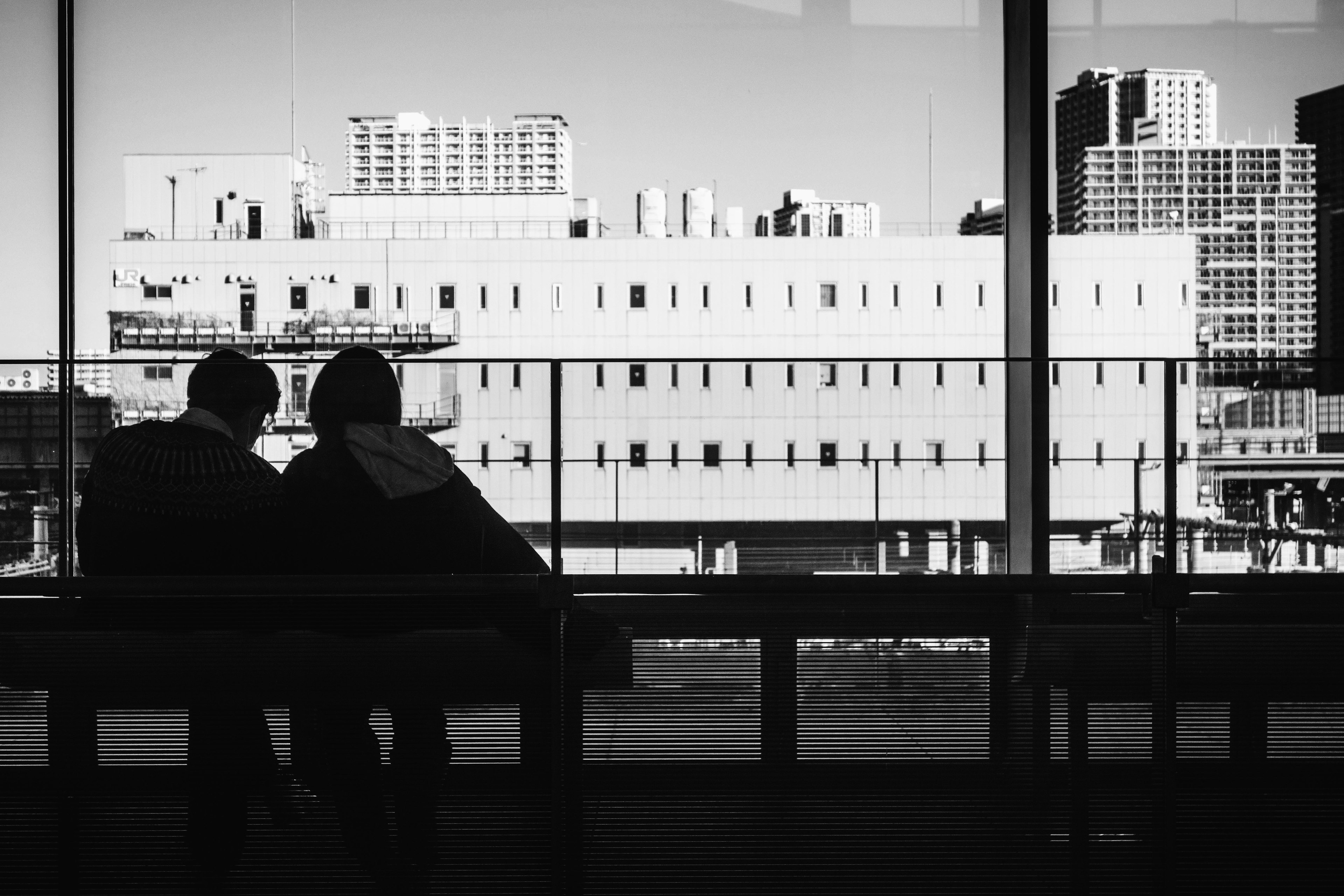 Deux personnes assises sur un banc regardant un paysage urbain à travers une fenêtre en noir et blanc