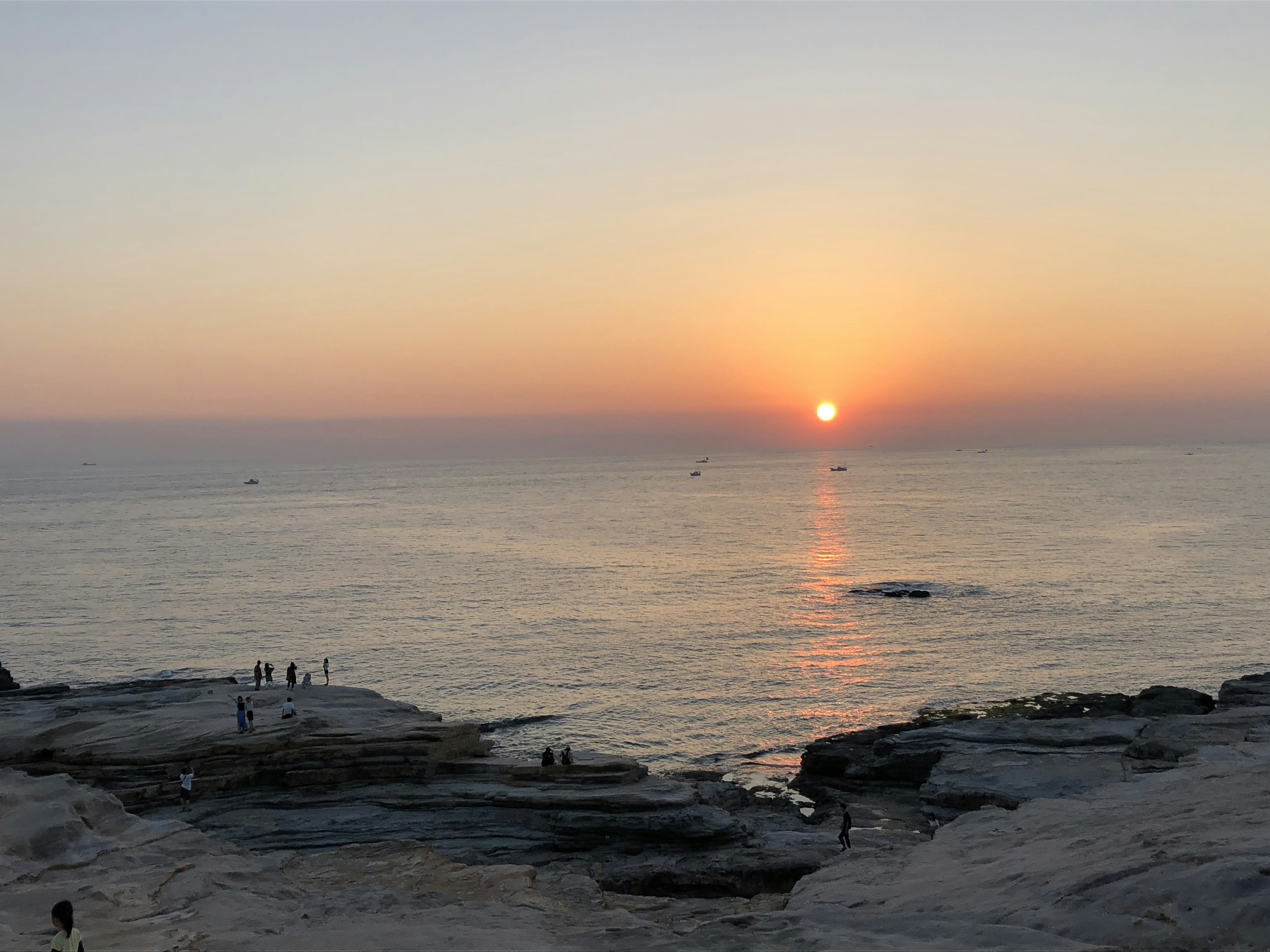 夕日が海に沈む美しい風景人々が岩の上に立っている