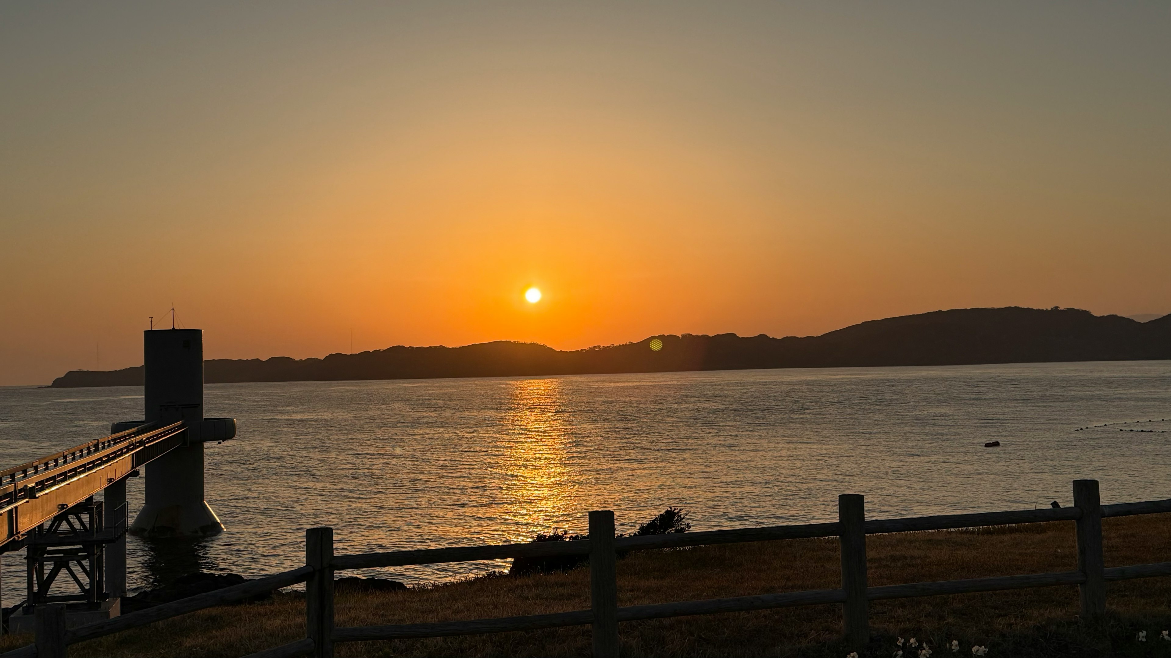 Un bel tramonto sul mare con un molo e colline sullo sfondo