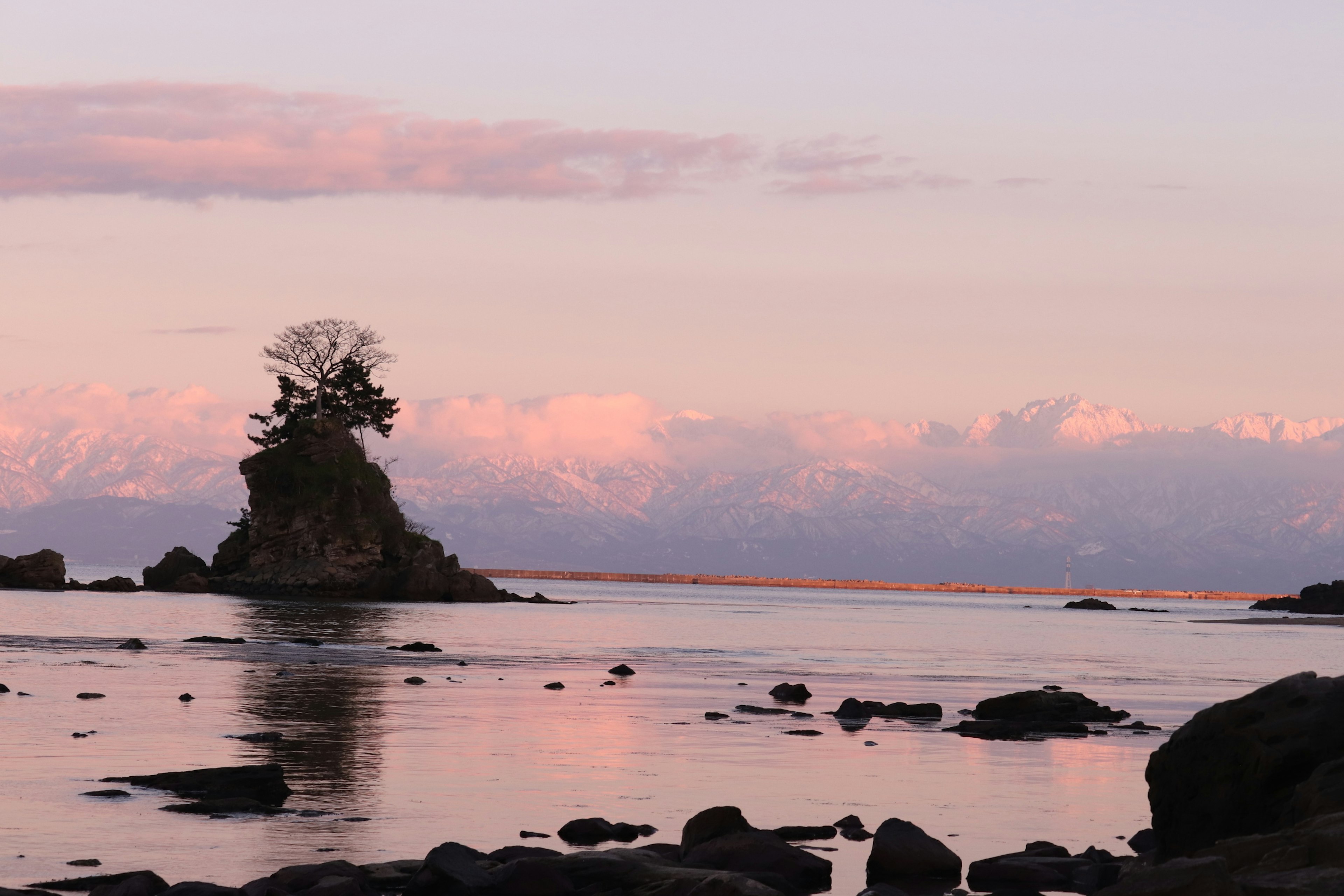 Une petite île avec des arbres au sommet entourée d'eaux calmes et de douces teintes de coucher de soleil