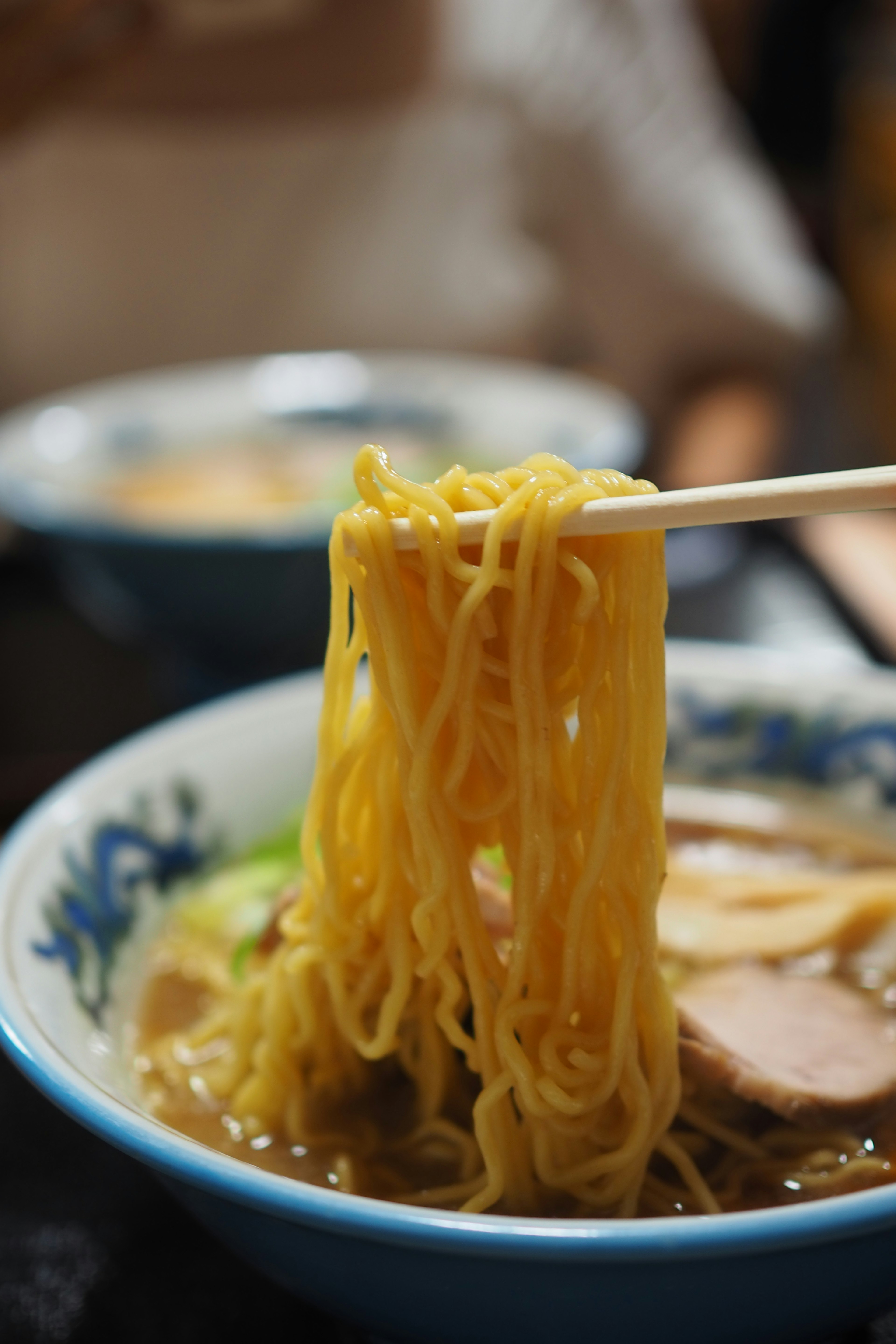 A close-up of noodles being lifted with chopsticks from a bowl of ramen