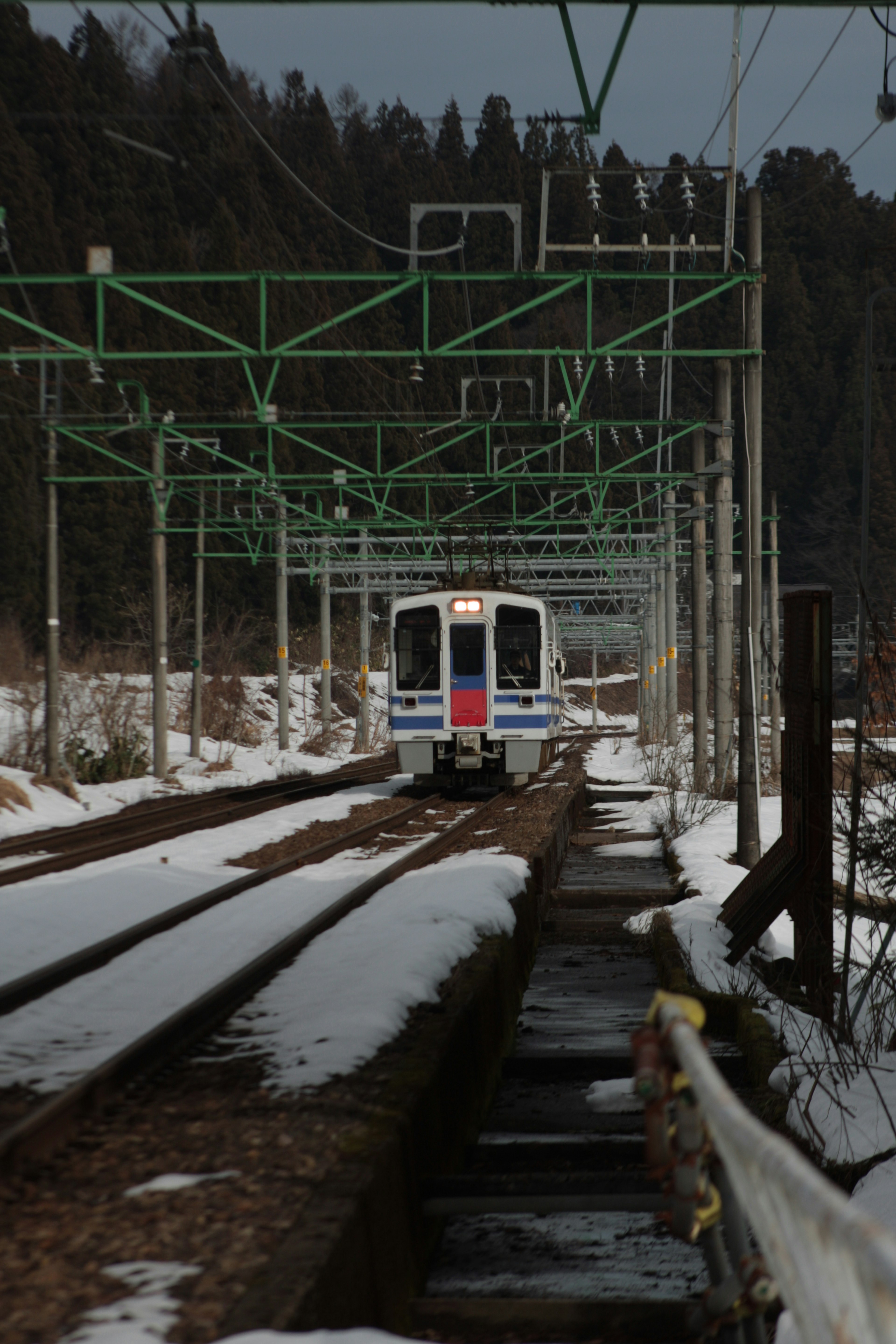 Zug, der durch Schnee fährt, mit grünen Oberleitungen