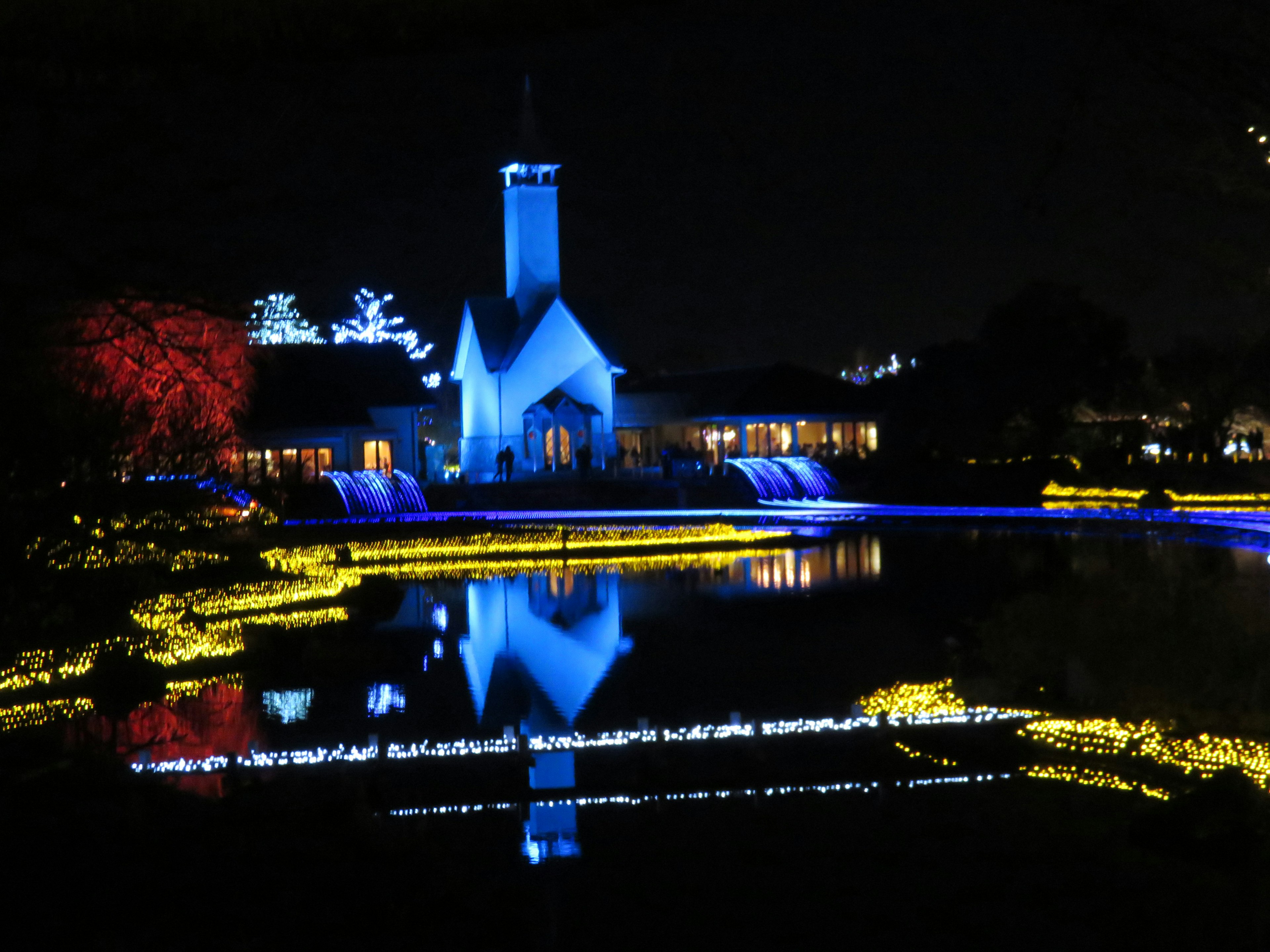 ทัศนียภาพสวยงามของโบสถ์ที่ถูกไฟสีน้ำเงินส่องสว่างในยามค่ำคืนพร้อมกับบ่อน้ำสะท้อน