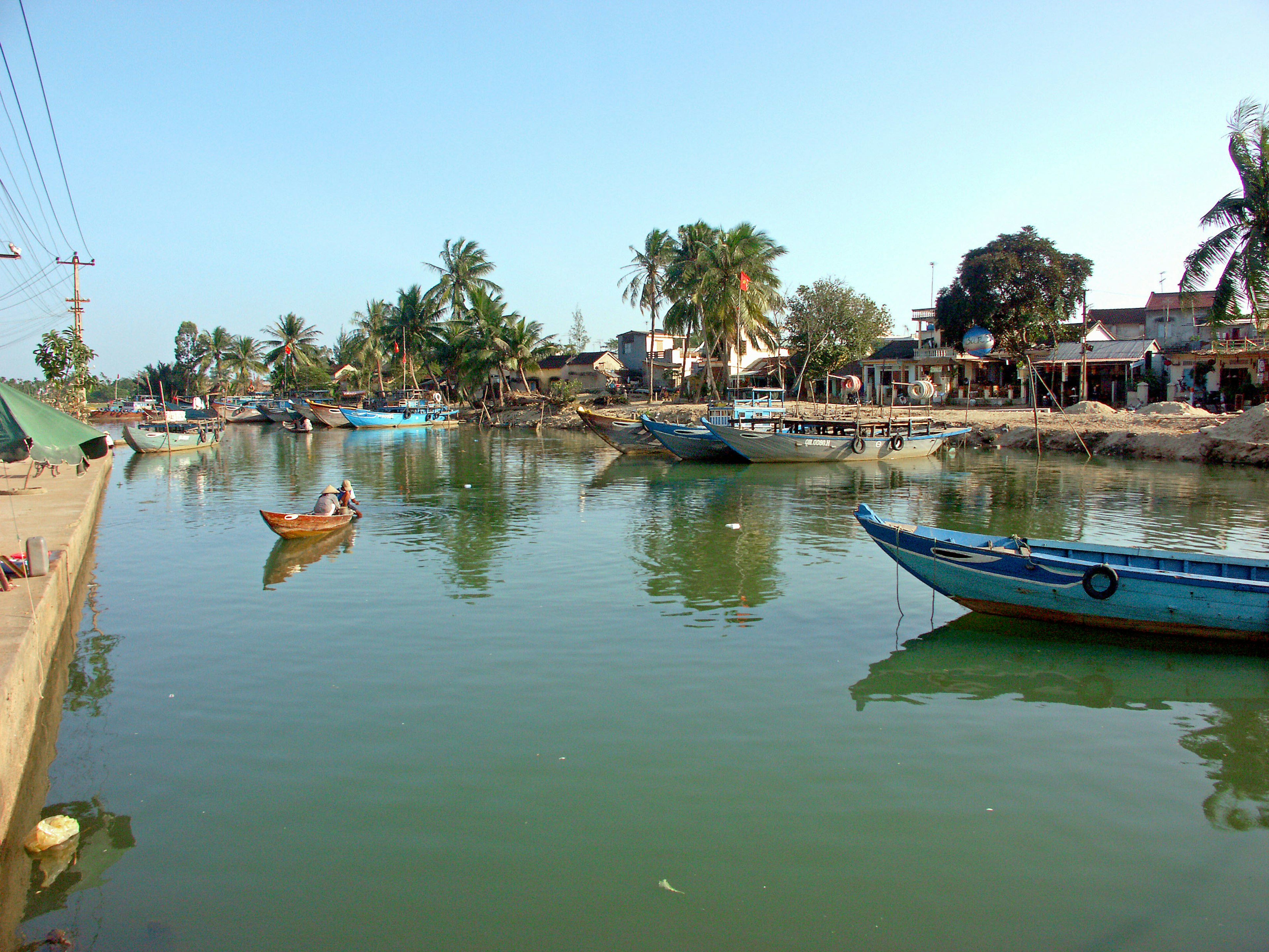 ทางน้ำที่เงียบสงบพร้อมเรือประมงและต้นไม้เขียวขจีรอบๆ