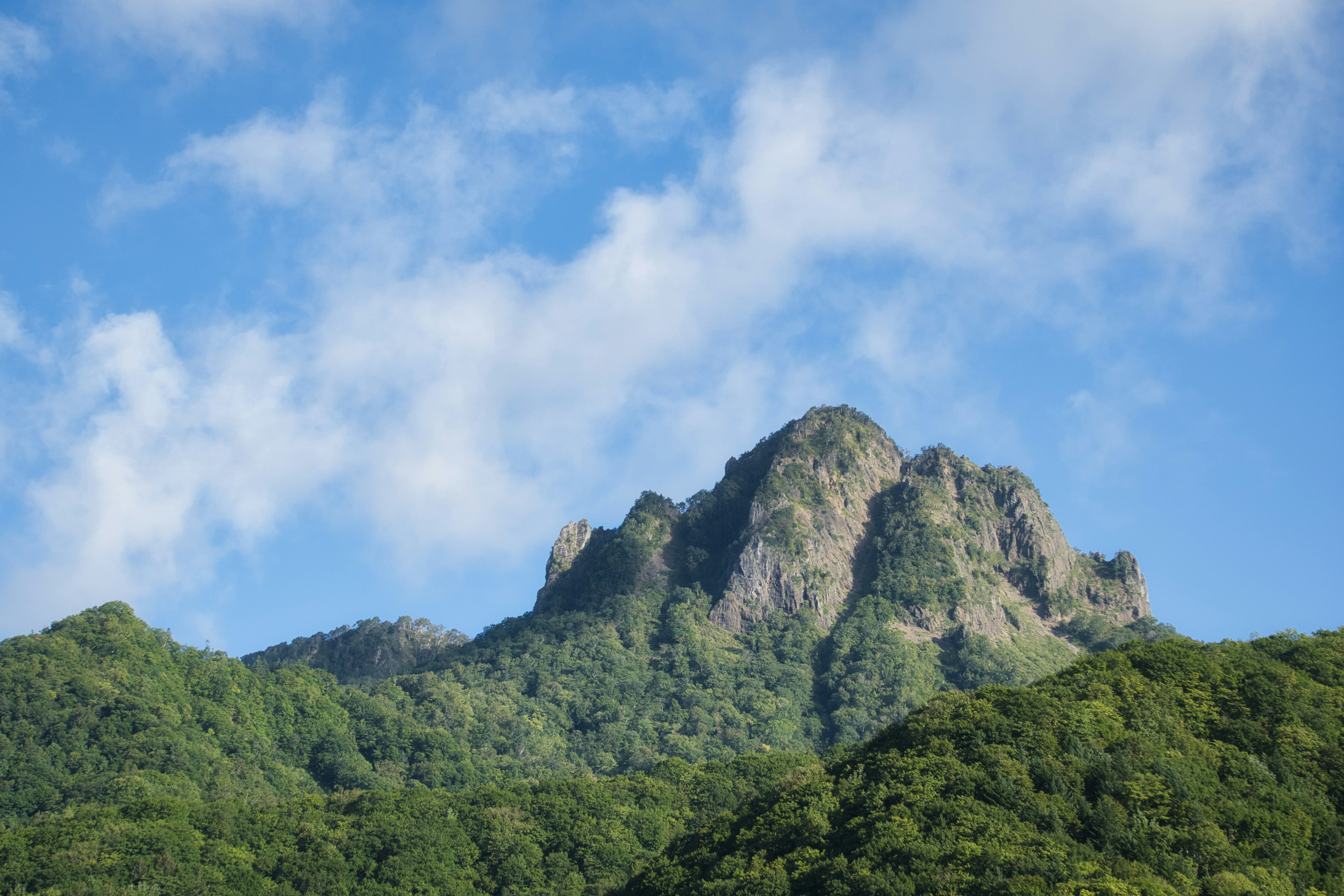 Pico montañoso verde bajo un cielo azul con nubes