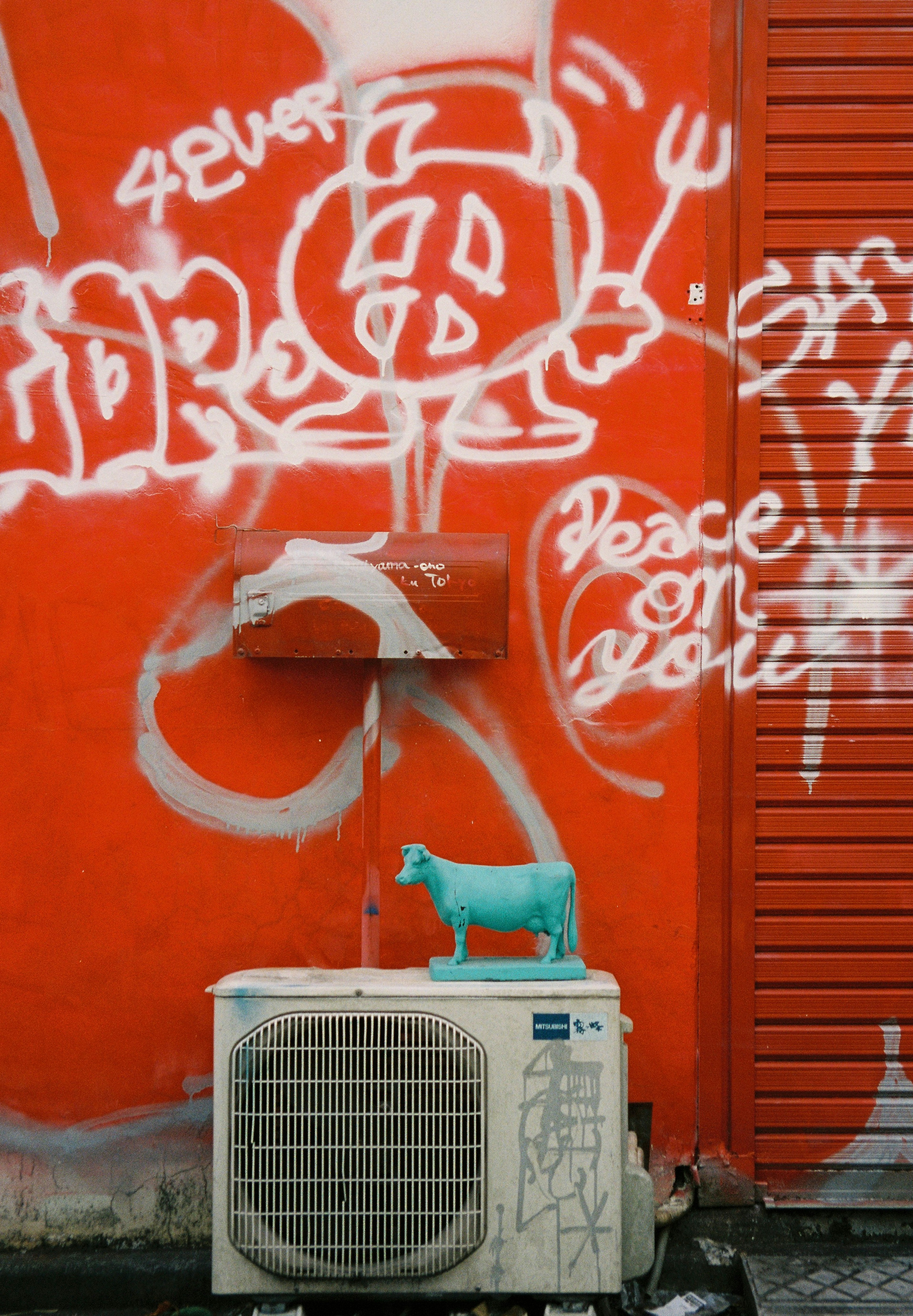 Une figurine de chien en plastique bleu sur une unité de climatisation contre un mur de graffiti orange