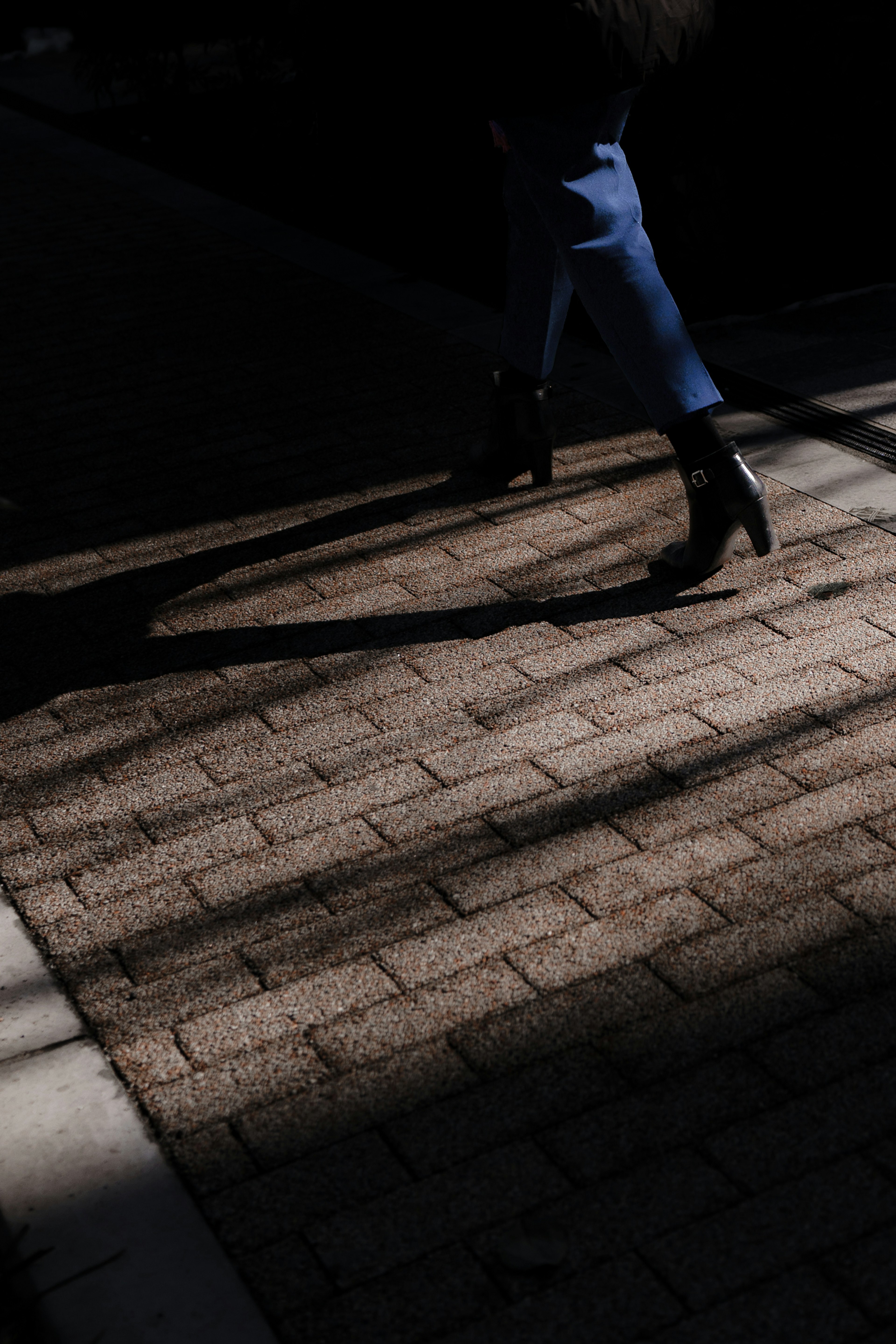 A person's feet walking in shadows on a cobblestone path