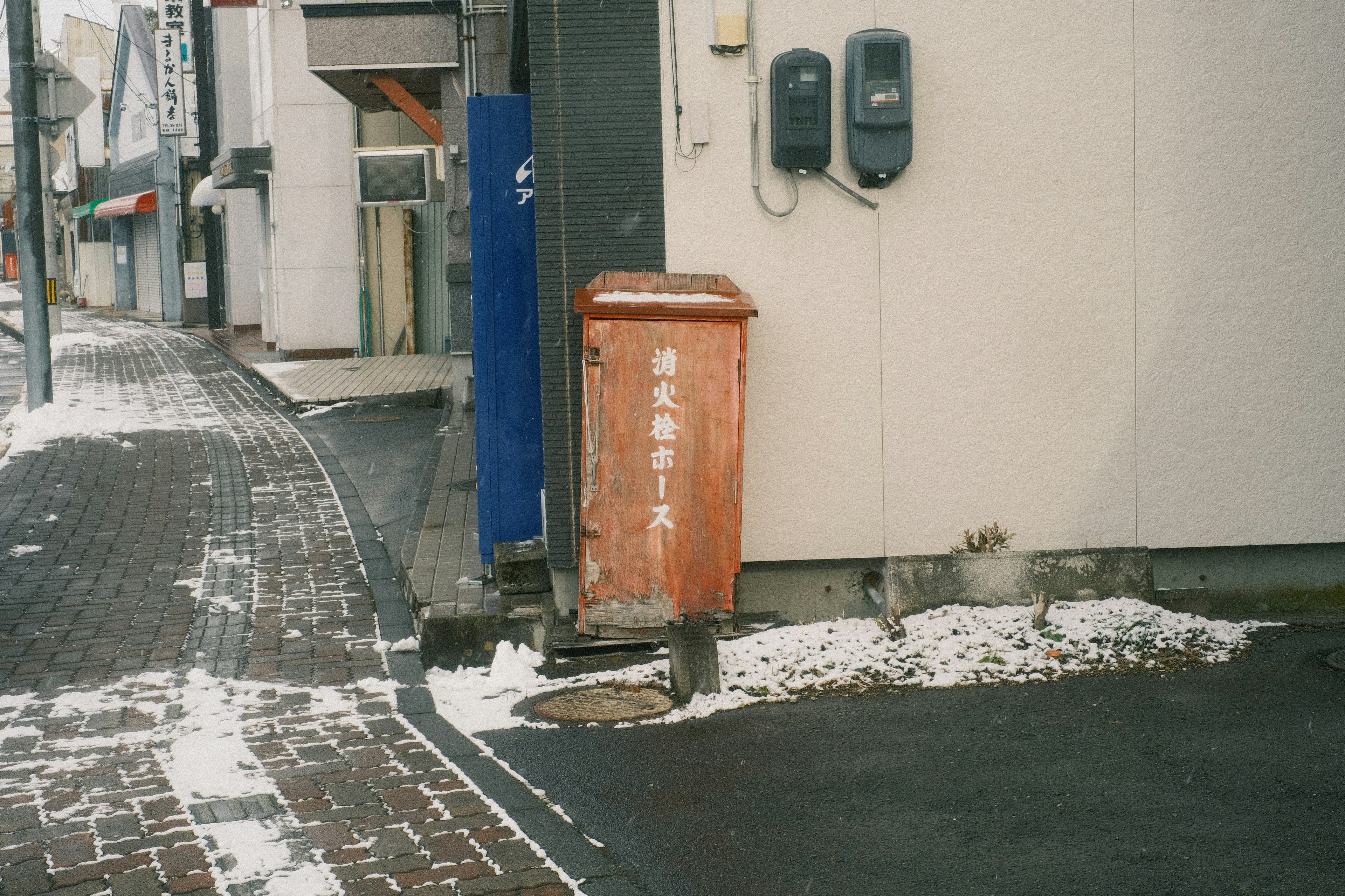 雪のある舗道に置かれたオレンジ色の郵便ポストと周囲の建物