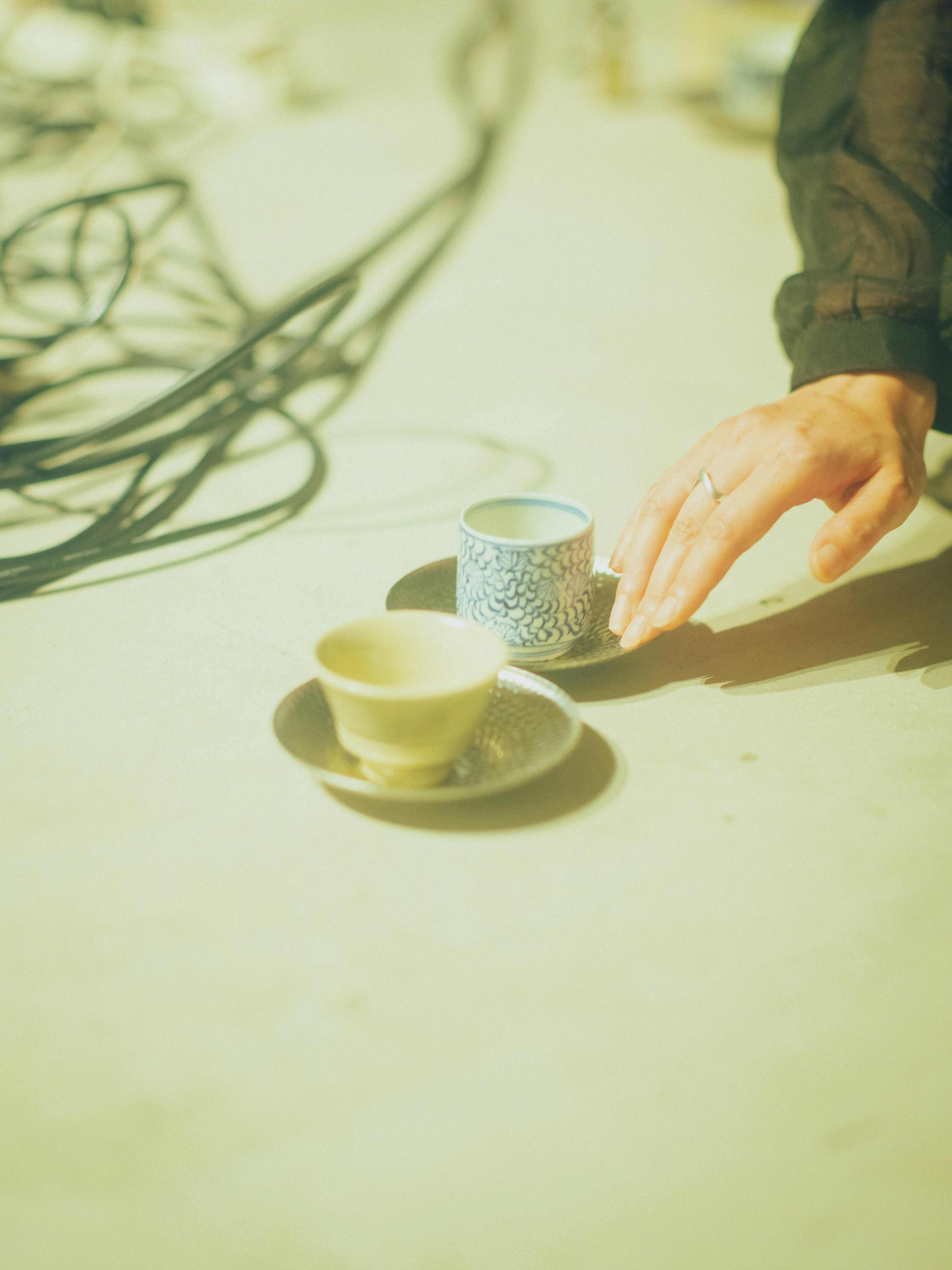 Una mano che si avvicina a una tazza blu a motivi su un piattino accanto a una tazza chiara su una superficie