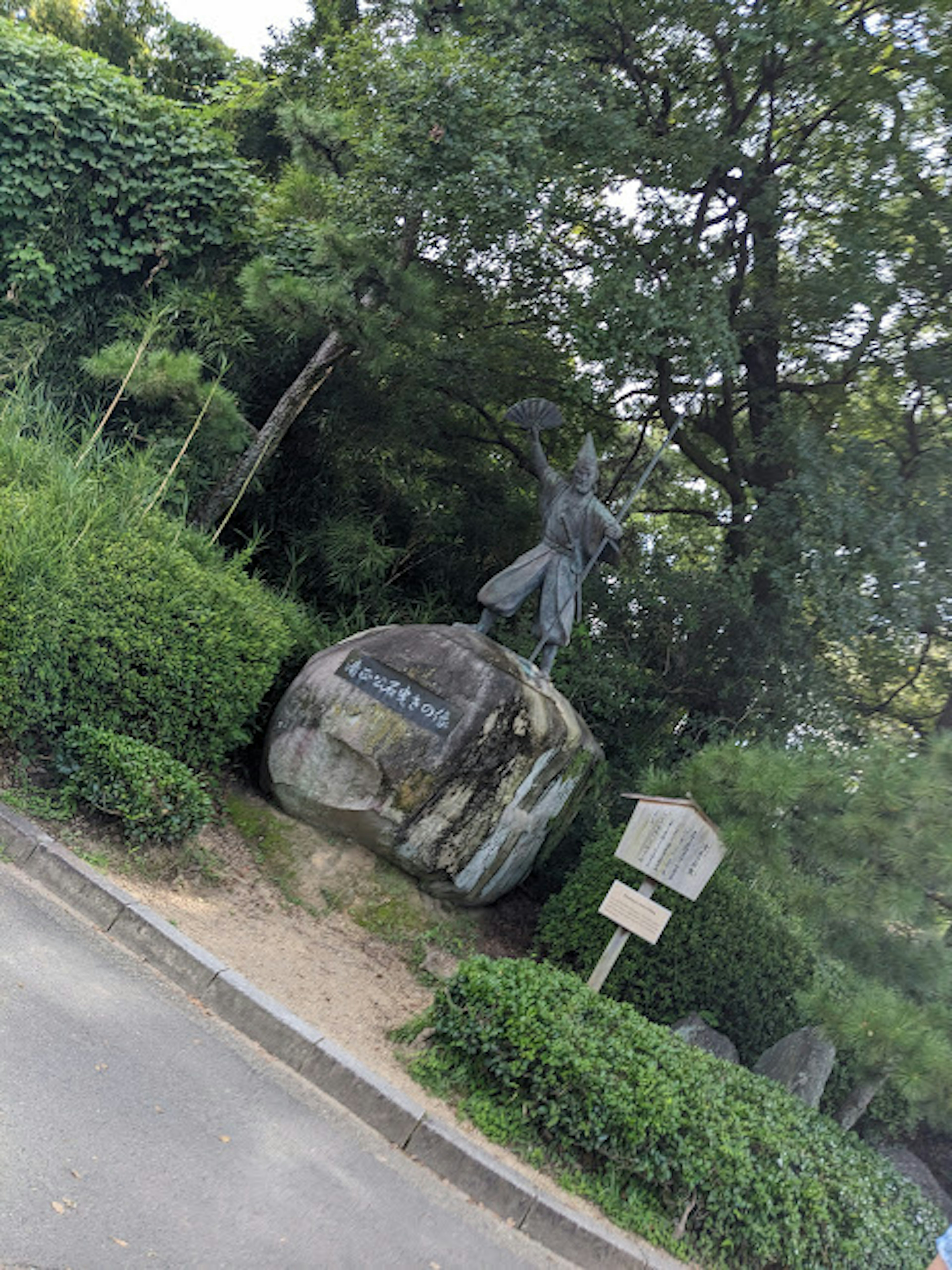 A sculpture standing on a stone surrounded by greenery