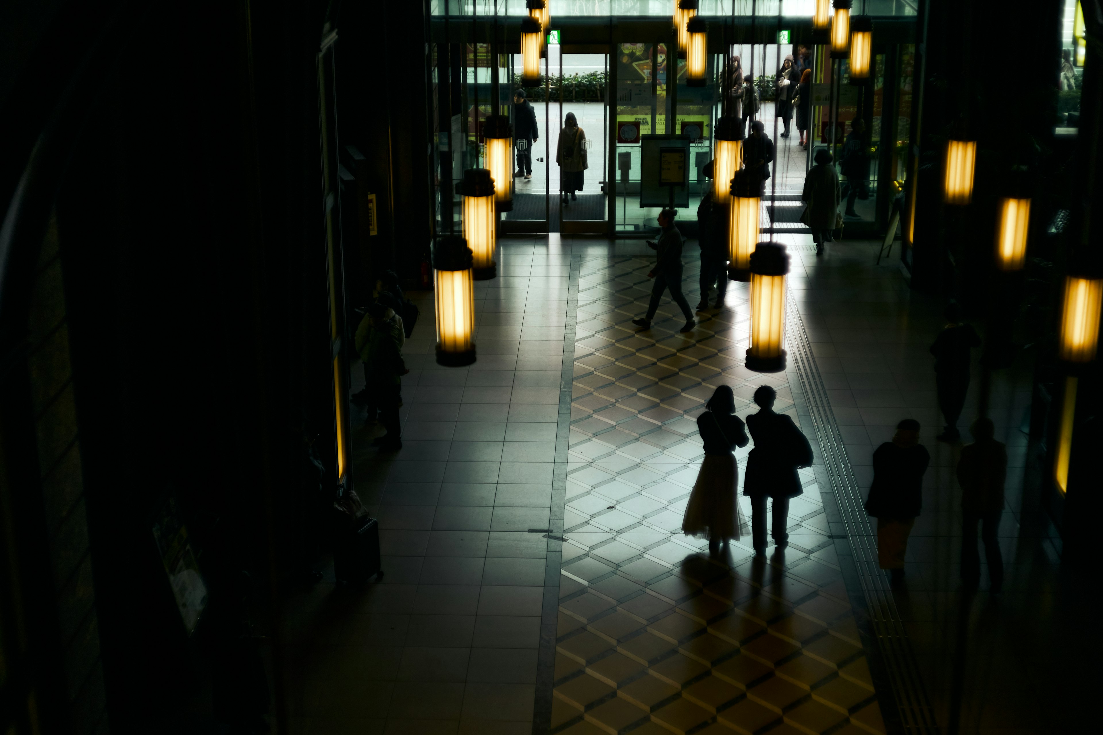 Menschen stehen in einer schwach beleuchteten Lobby Silhouetten und hängende Lampen sind hervorstechend