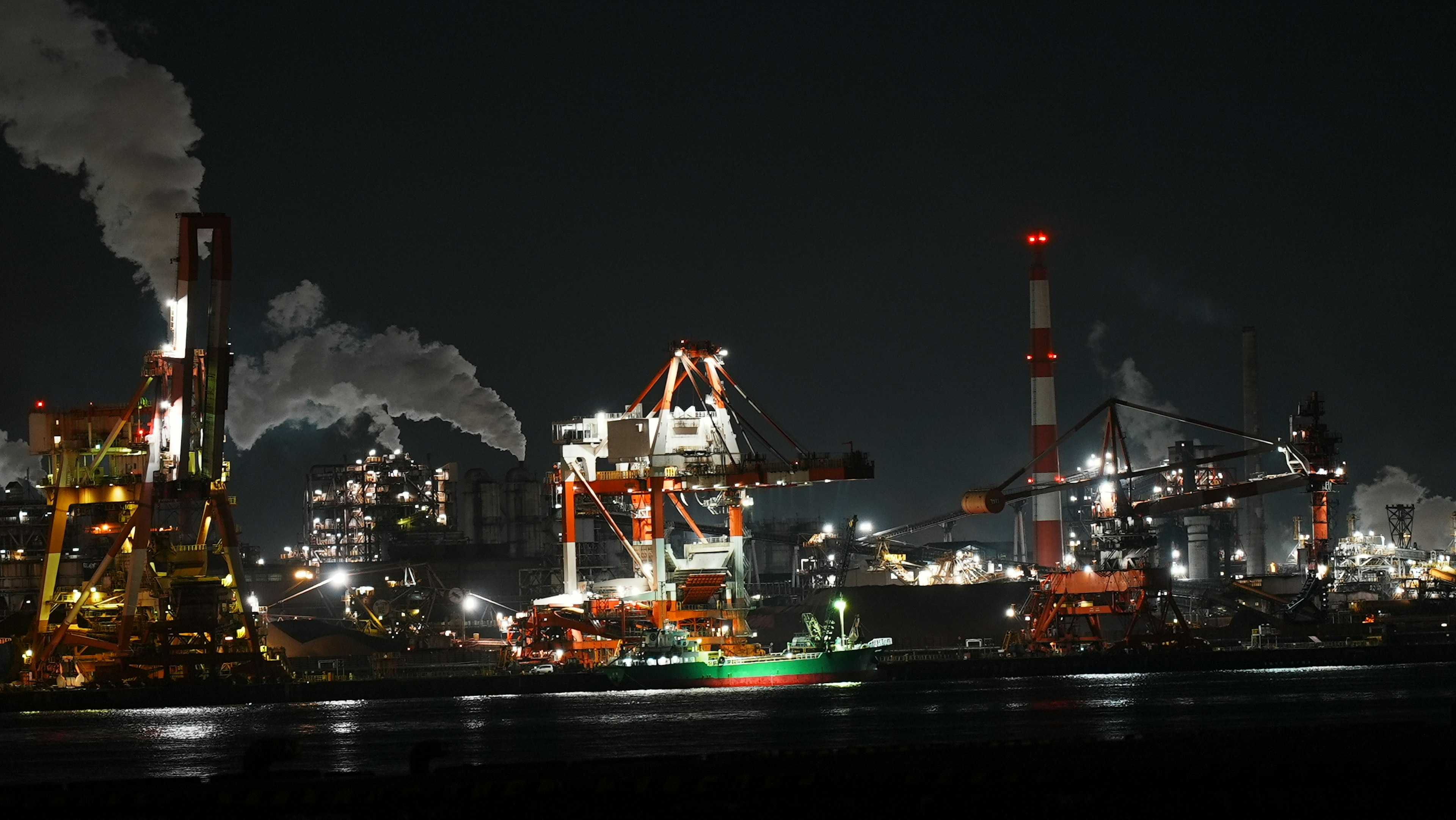 Industrial area at night with cranes and smokestacks visible