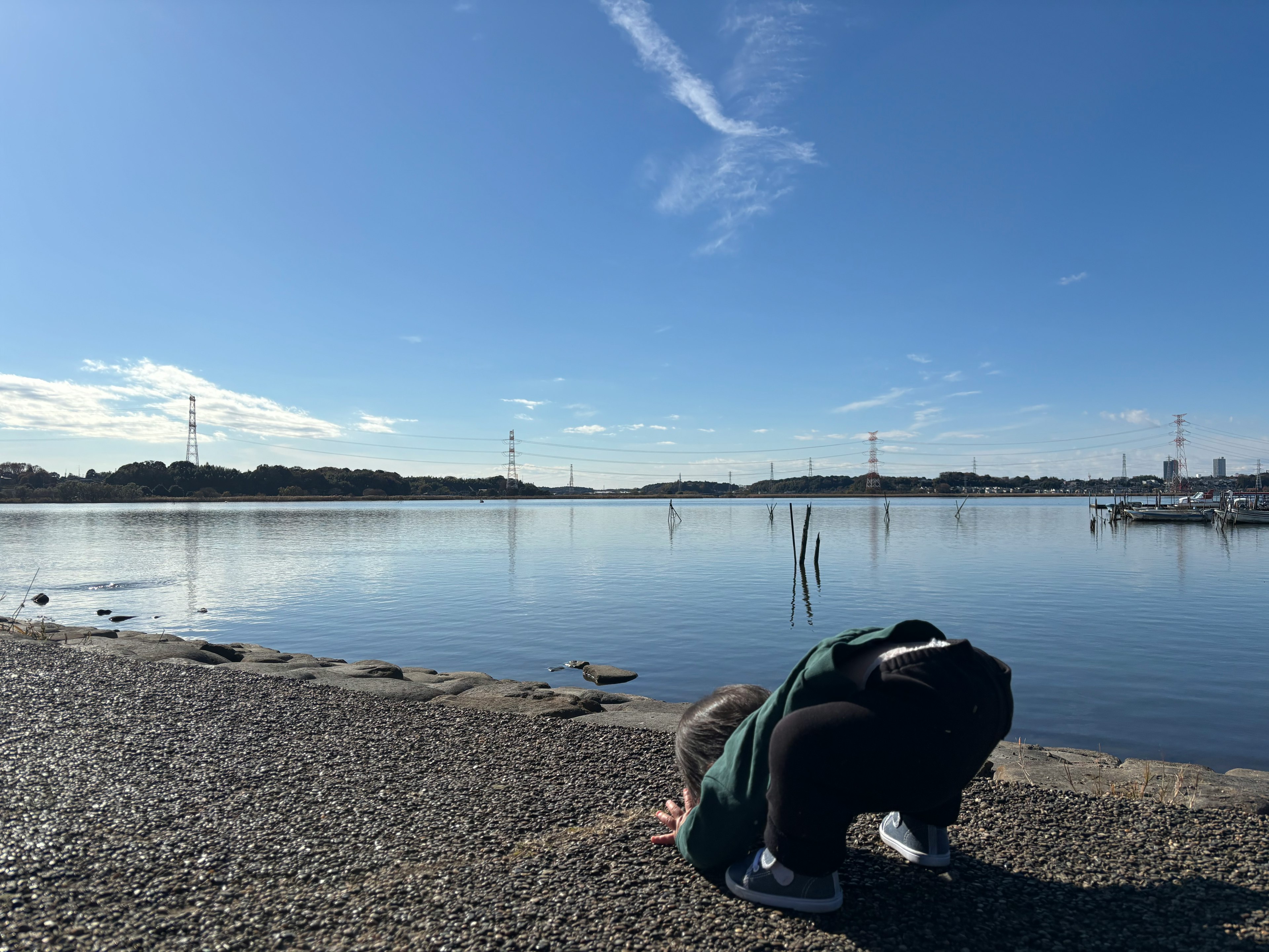 Person crouching by the water under a blue sky