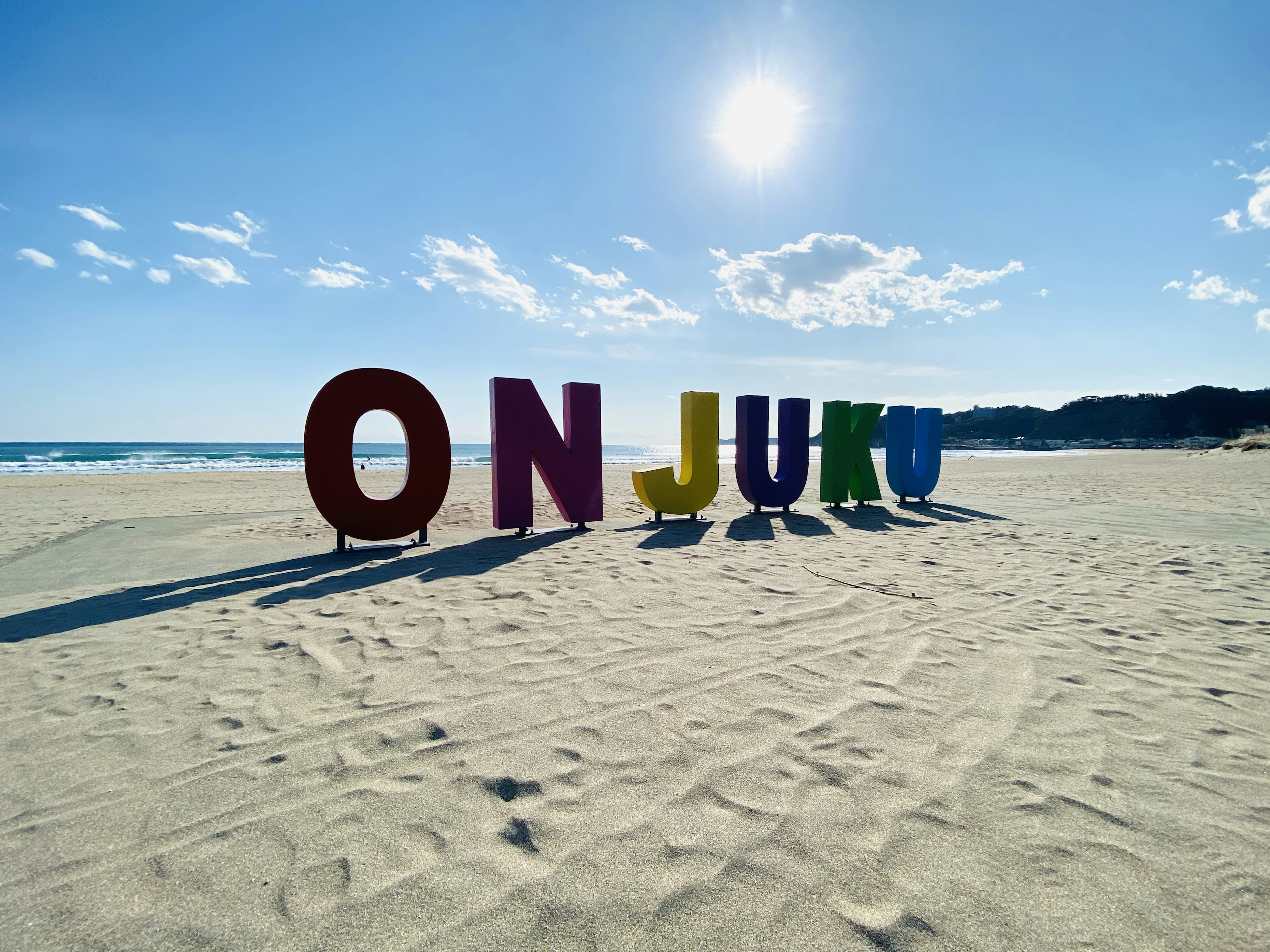 Lettres colorées épelant 'ON JURU' sur une plage de sable sous un ciel ensoleillé