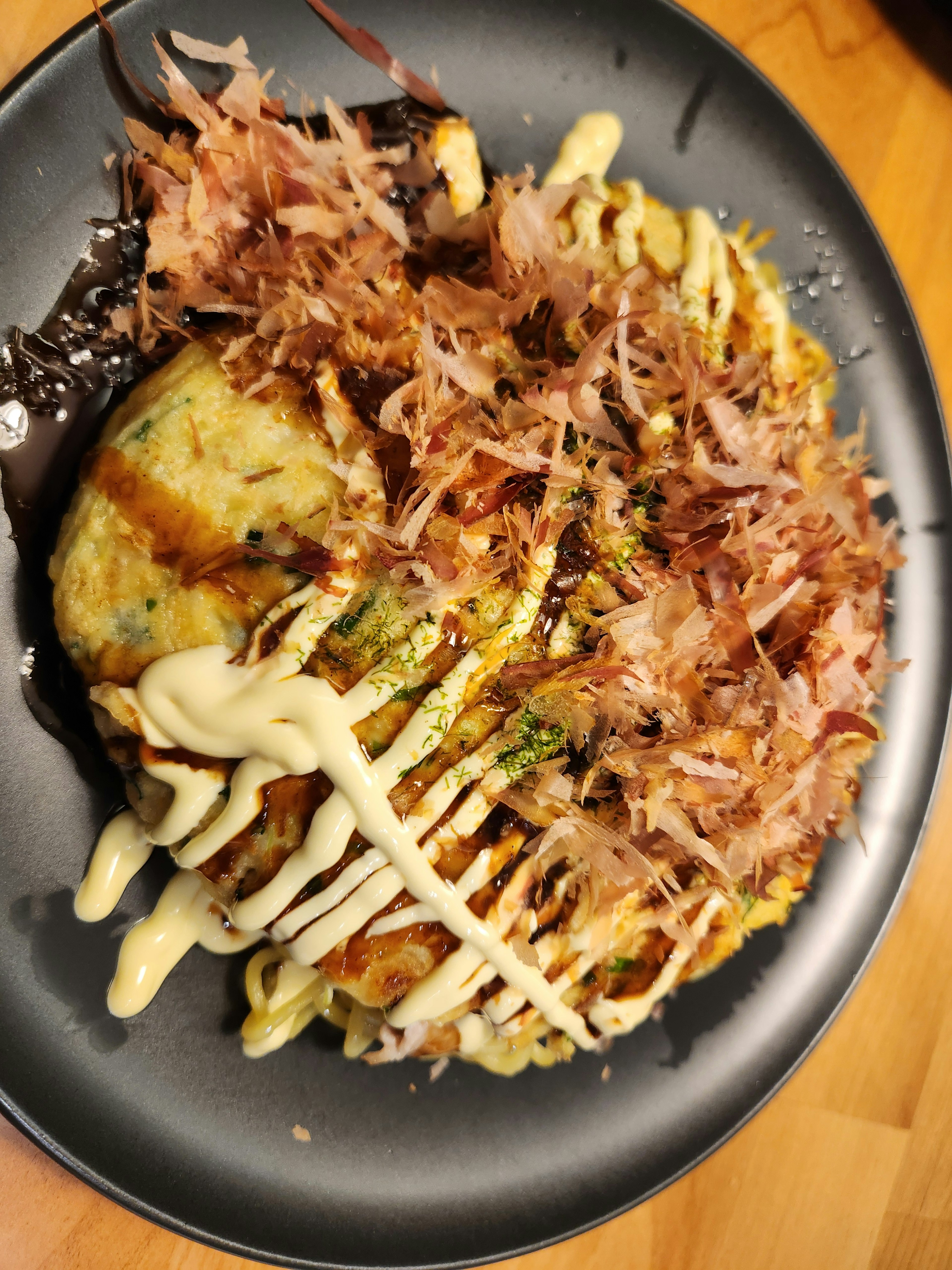 Okonomiyaki topped with bonito flakes and mayonnaise on a black plate