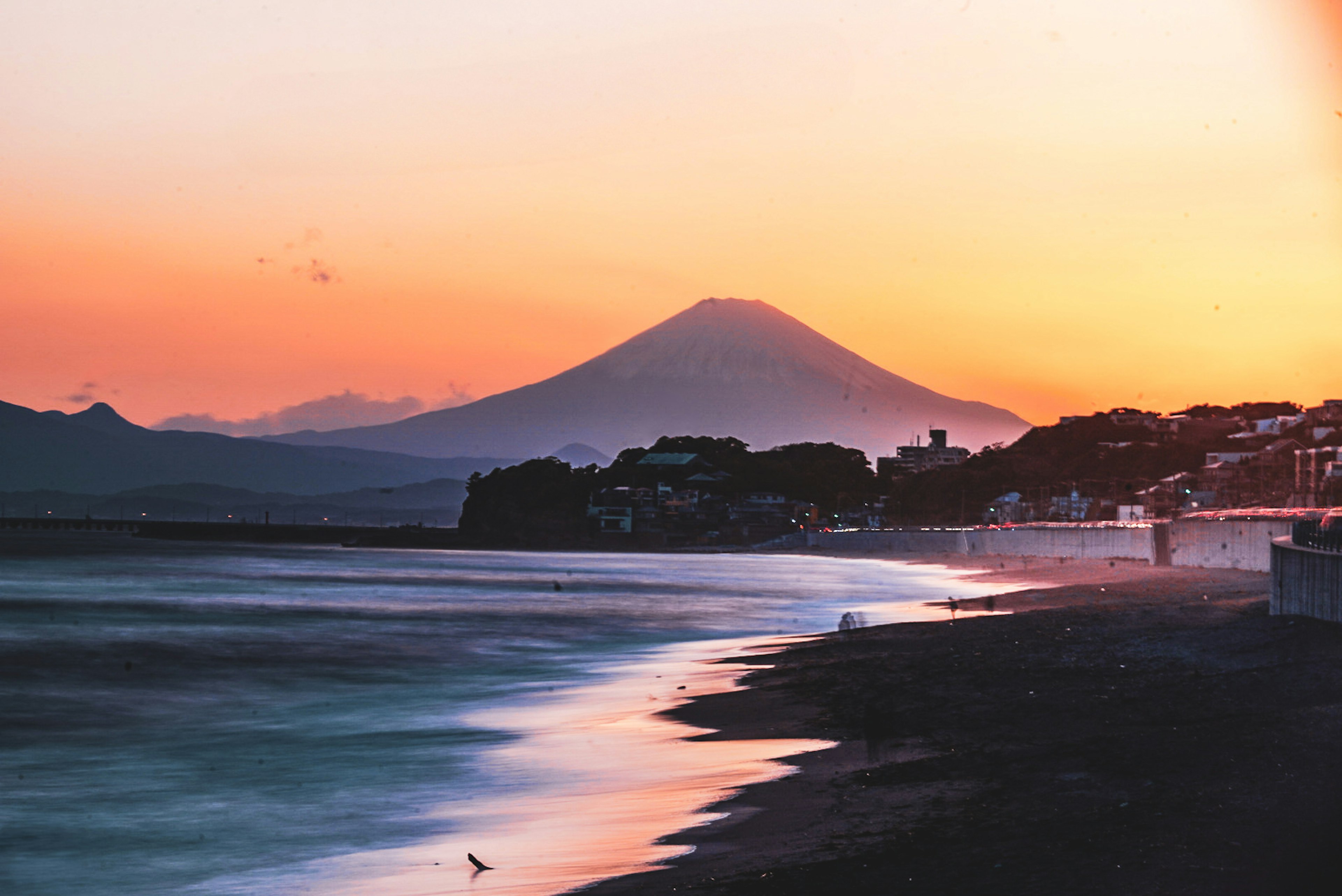 Le mont Fuji s'élevant majestueusement contre un coucher de soleil vibrant et une côte tranquille