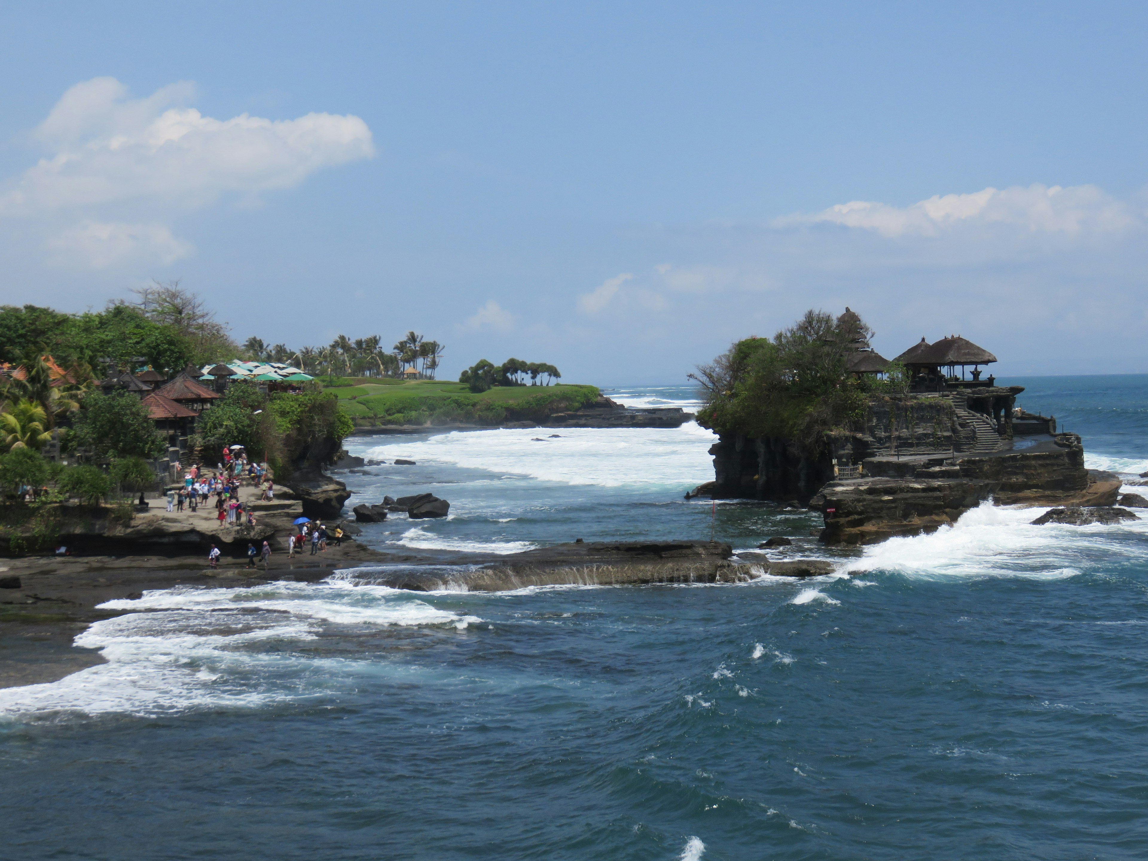 Coastal view of Tanah Lot Temple in Bali with crashing waves and lush greenery