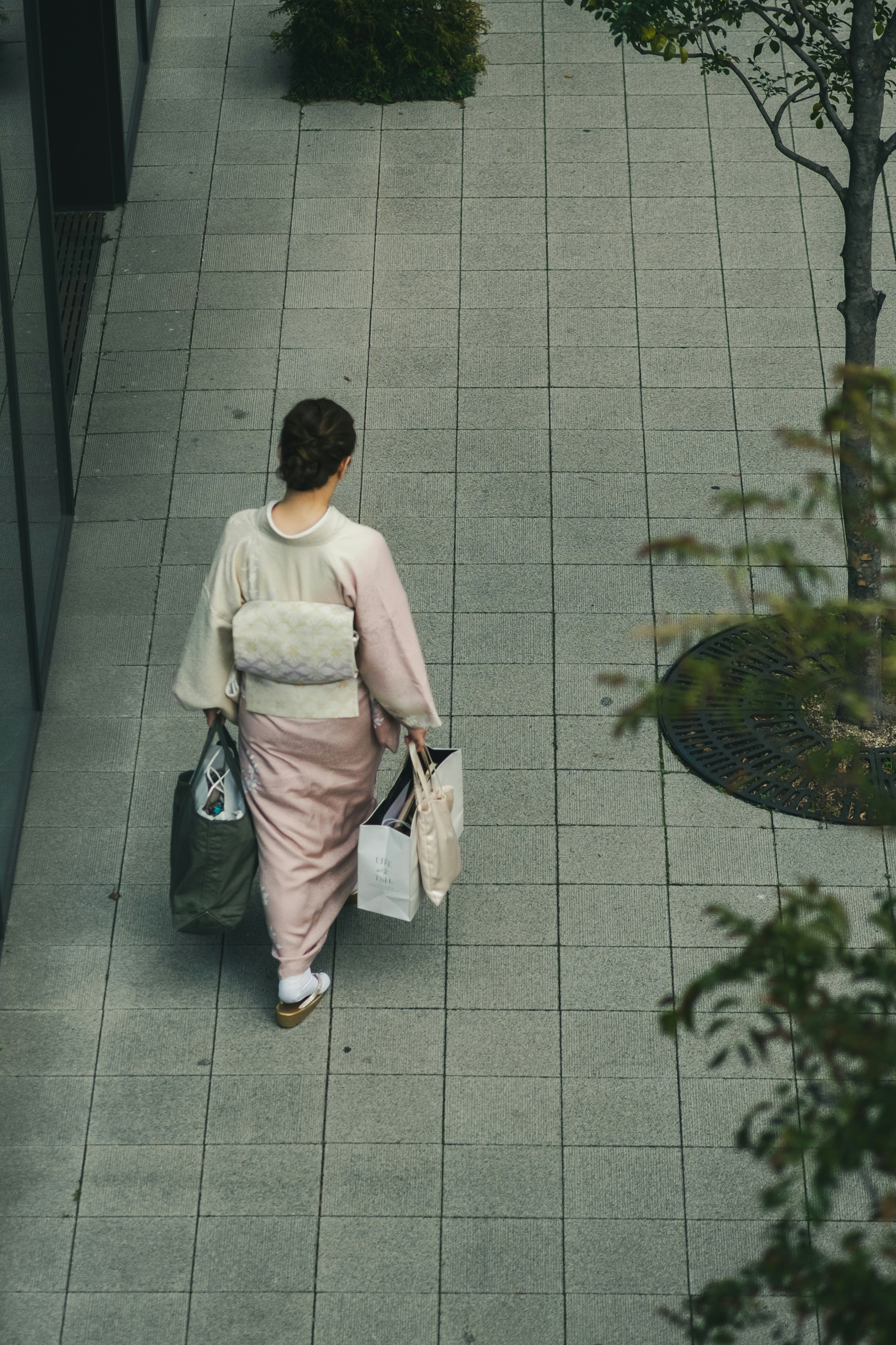 연한 분홍색 기모노를 입은 여성이 쇼핑 가방을 들고 타일 길을 걷고 있다