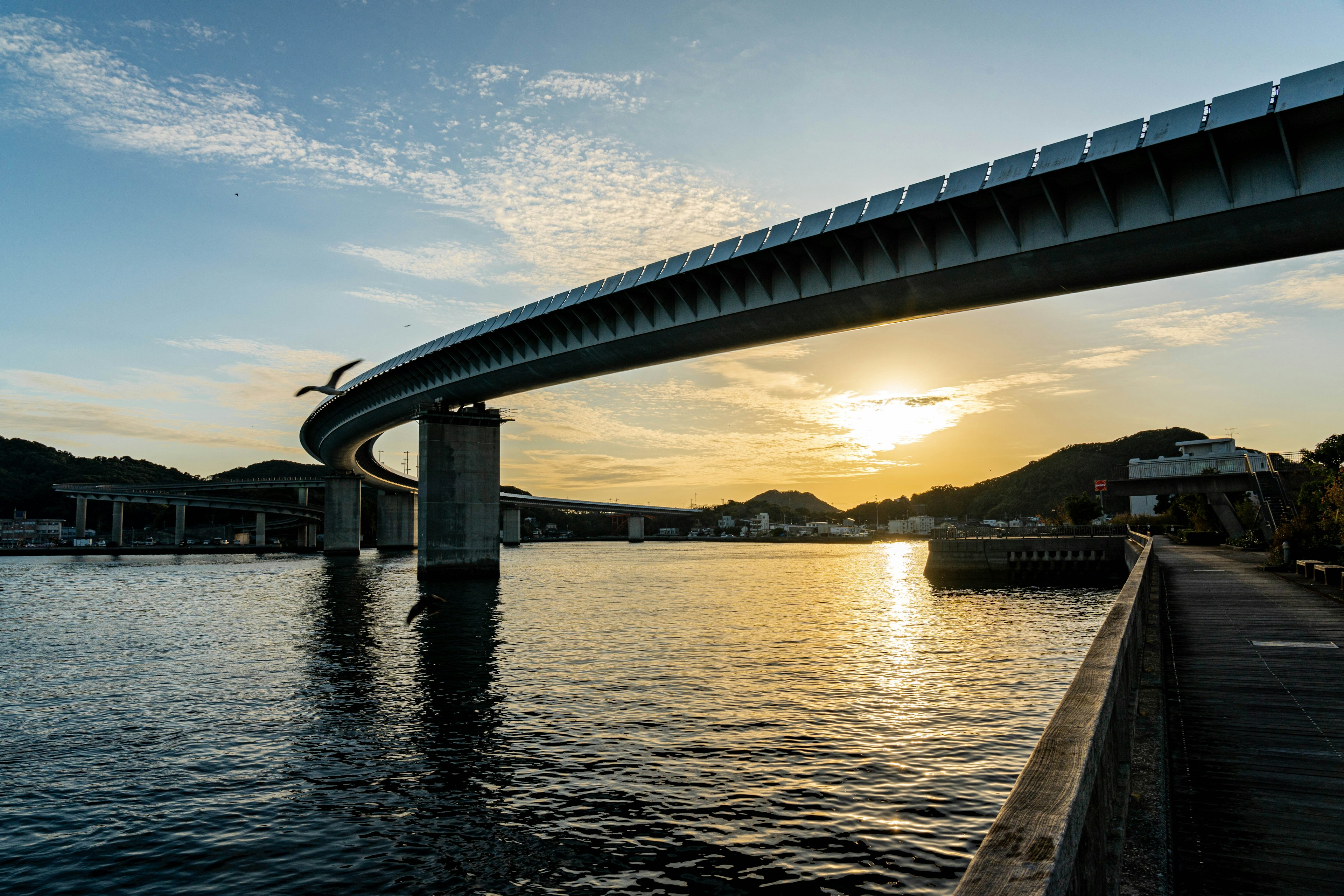 Modern bridge arching over a river at sunset